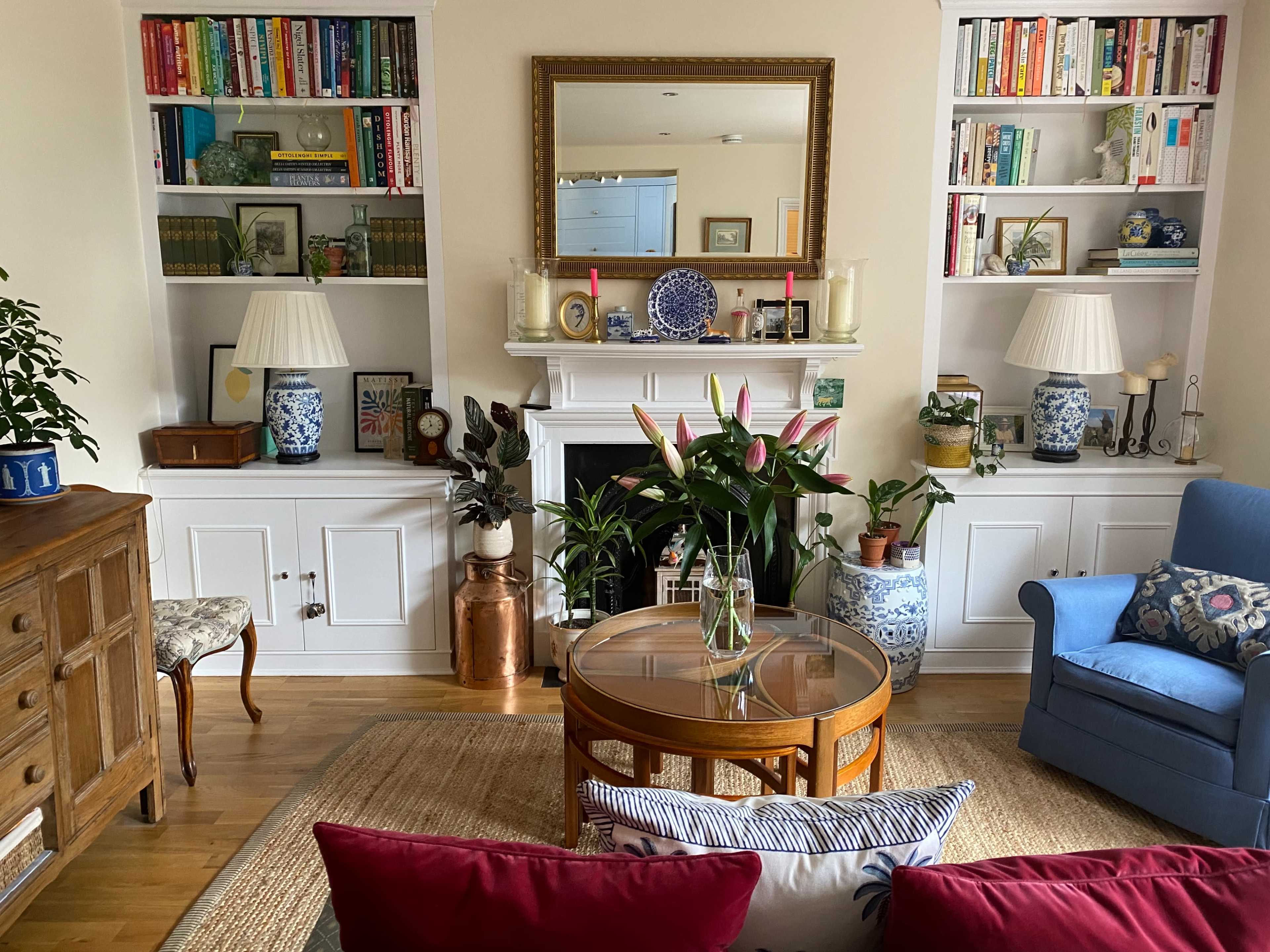 A cozy living room featuring a bookshelf filled with books, a fireplace with decorative items, and a coffee table surrounded by a sofa and chairs.