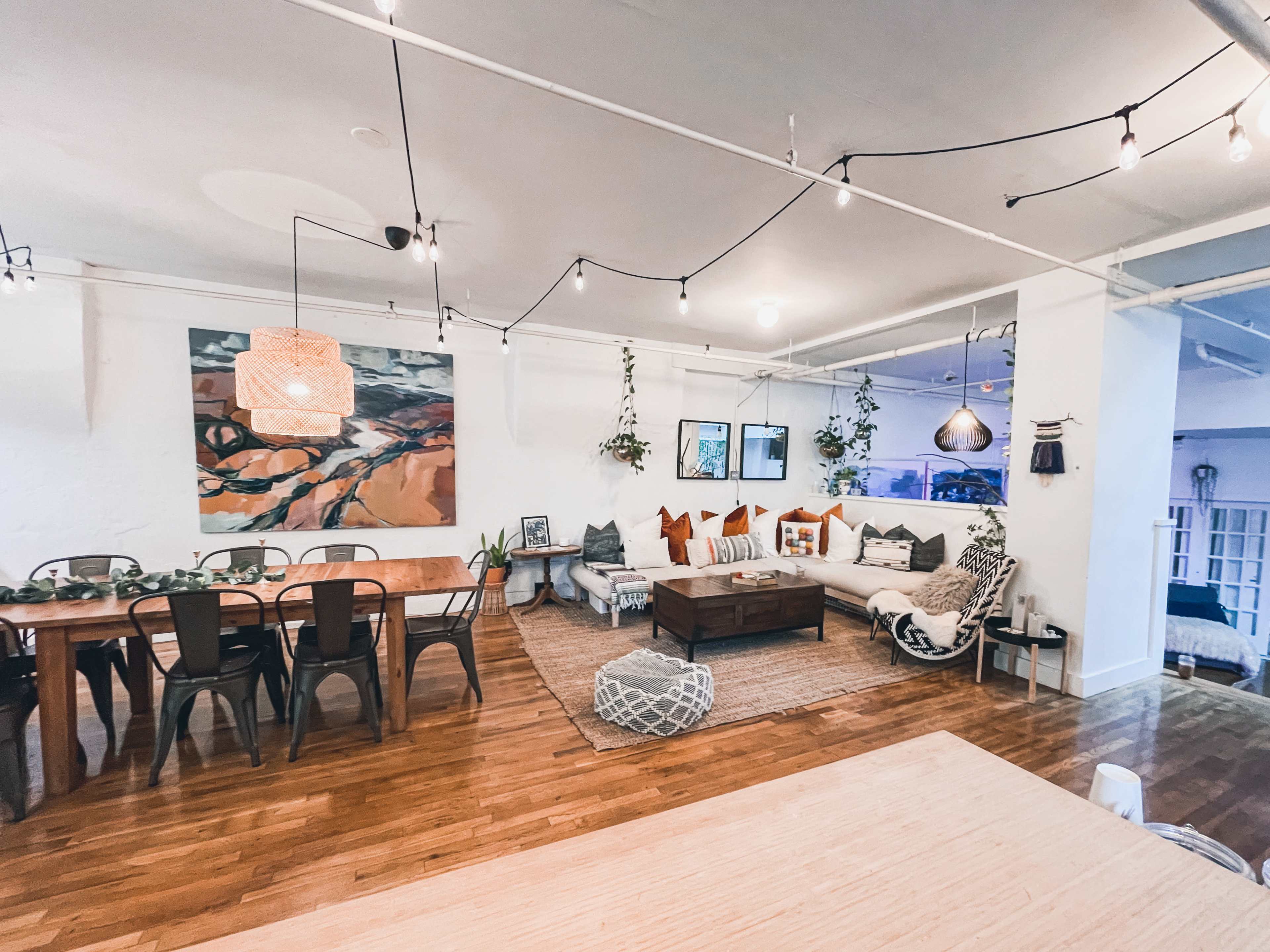 A spacious, modern living area with a large sectional sofa, a wooden dining table, and decorative plants hanging from the ceiling.