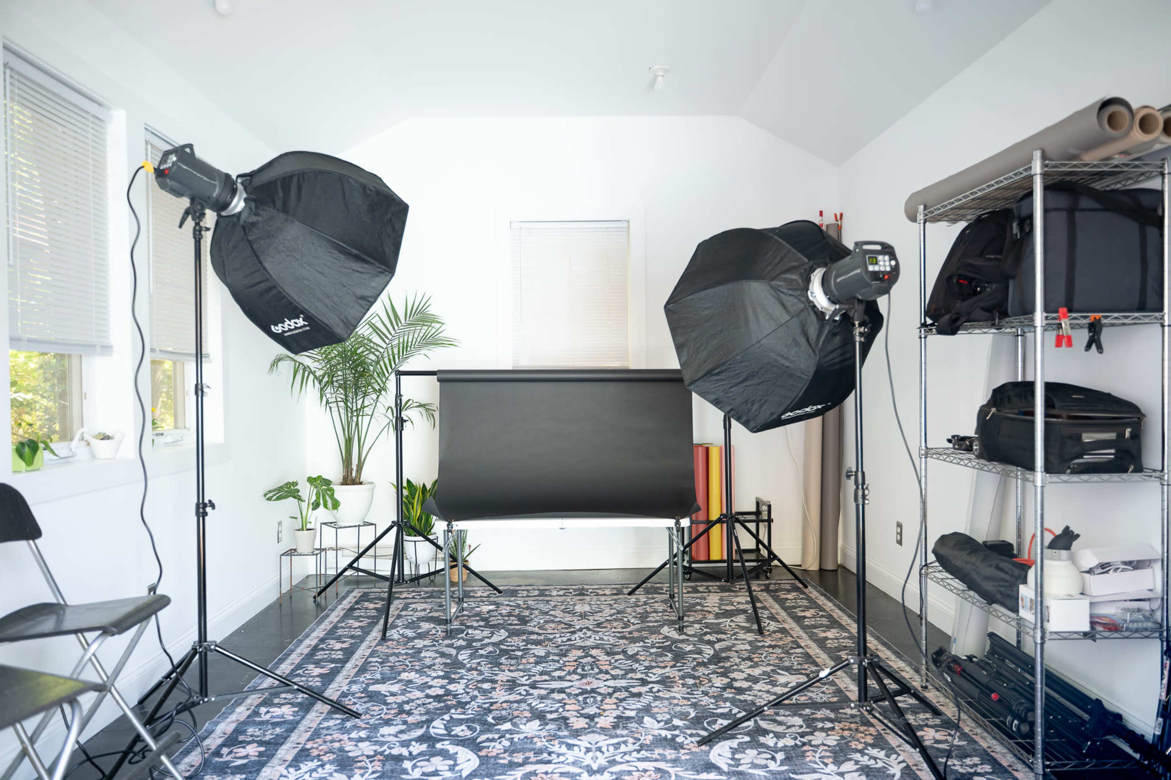 The image shows a photography studio setup with two softbox lights, a backdrop, and various equipment neatly arranged on shelves.