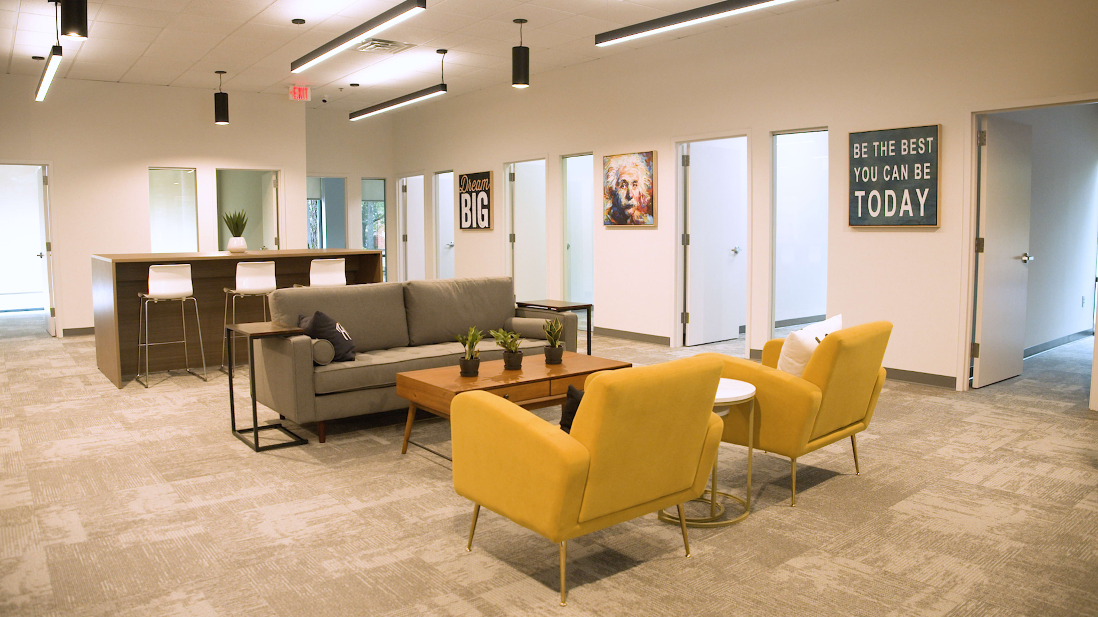 A modern office space featuring a gray sofa, yellow armchairs, a wooden coffee table, and several closed office doors in a brightly lit environment.