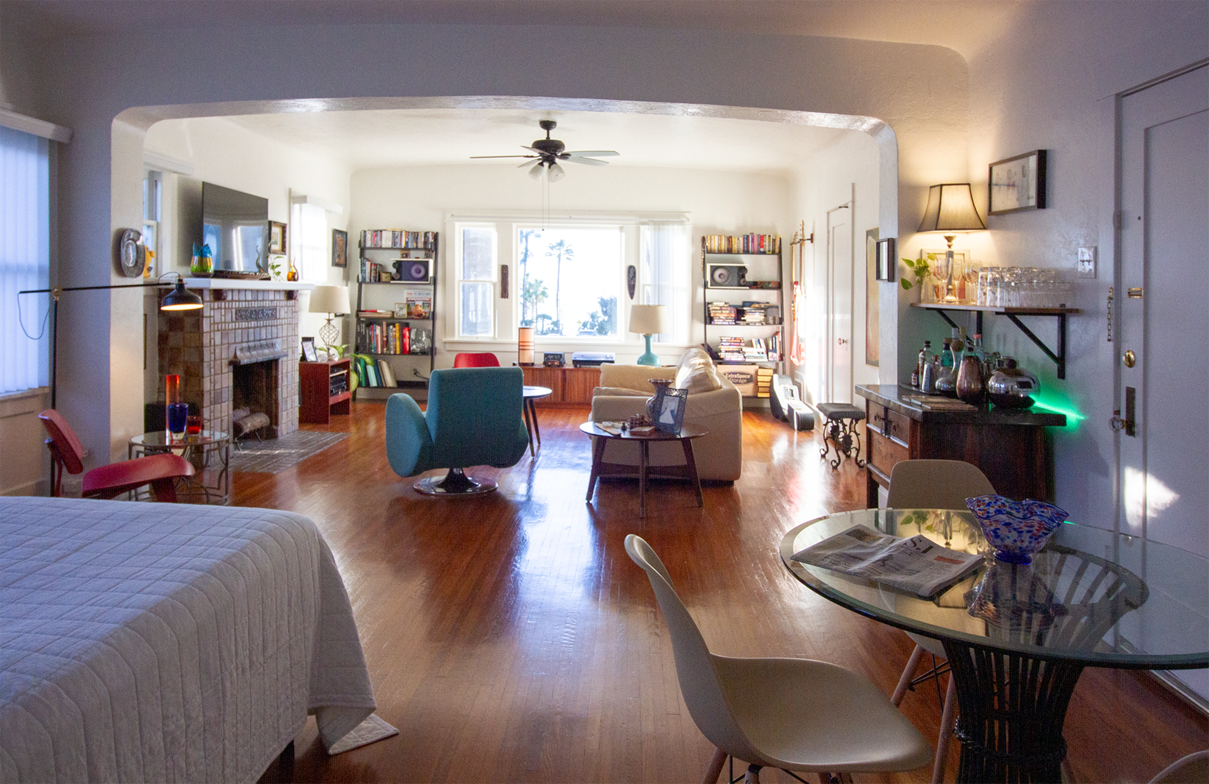 A spacious living area with a sitting area, a dining table, a fireplace, and bookshelves, all illuminated by natural light from large windows.