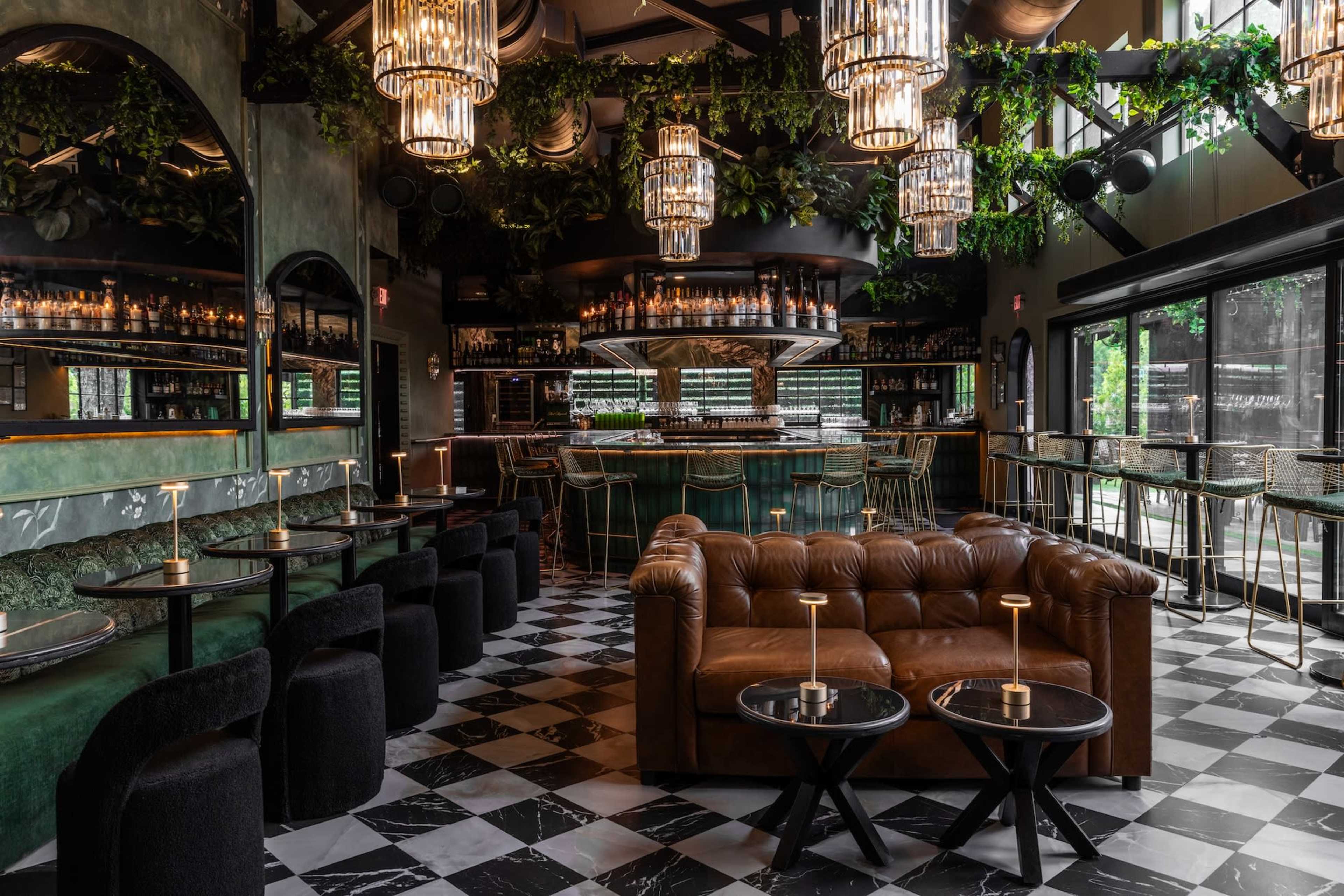 The image shows a stylish restaurant interior with a mix of dark and light furnishings, featuring a plush leather sofa, contemporary lighting fixtures, and a checkered floor.