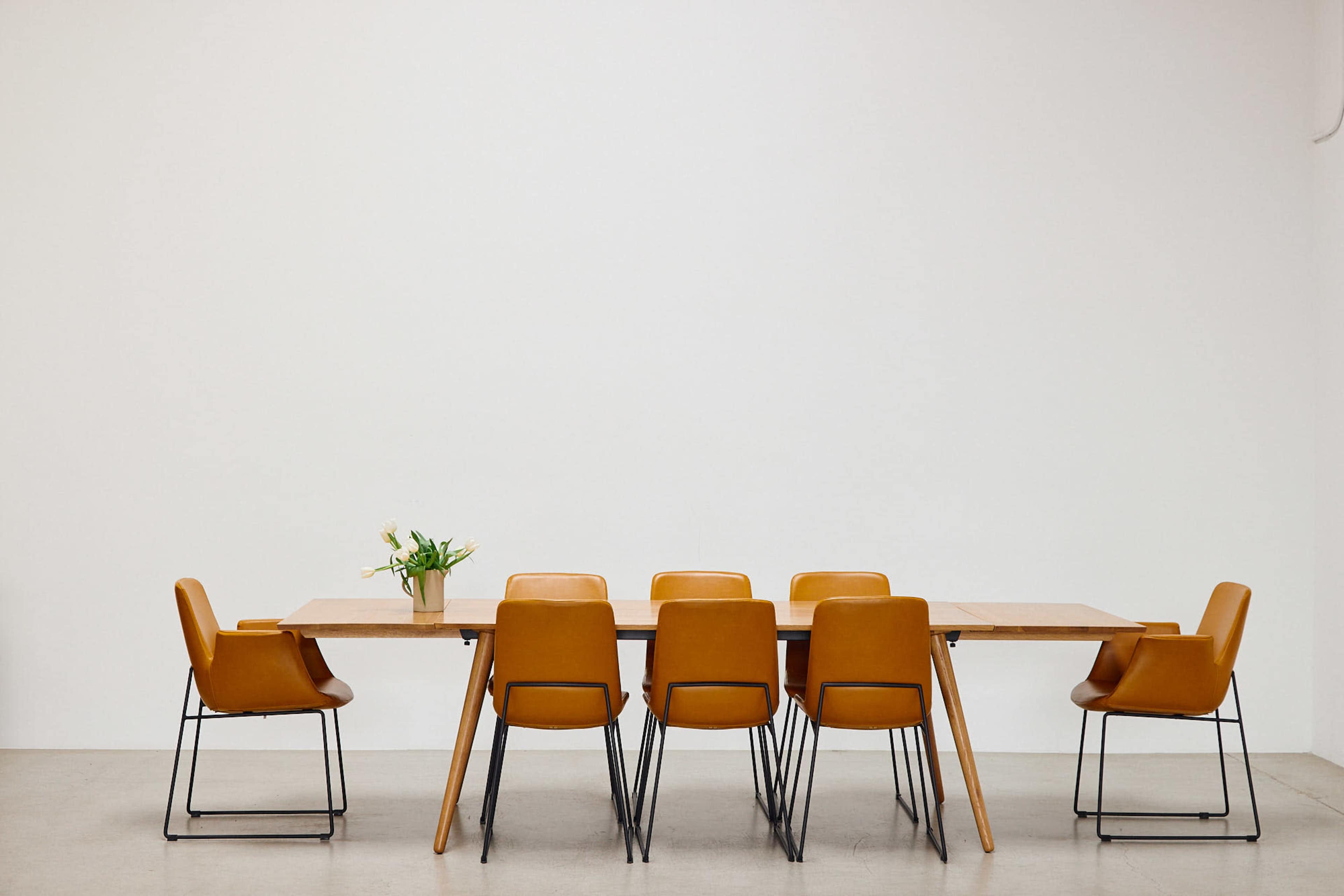 A wooden dining table with six yellow chairs is positioned against a plain white wall.