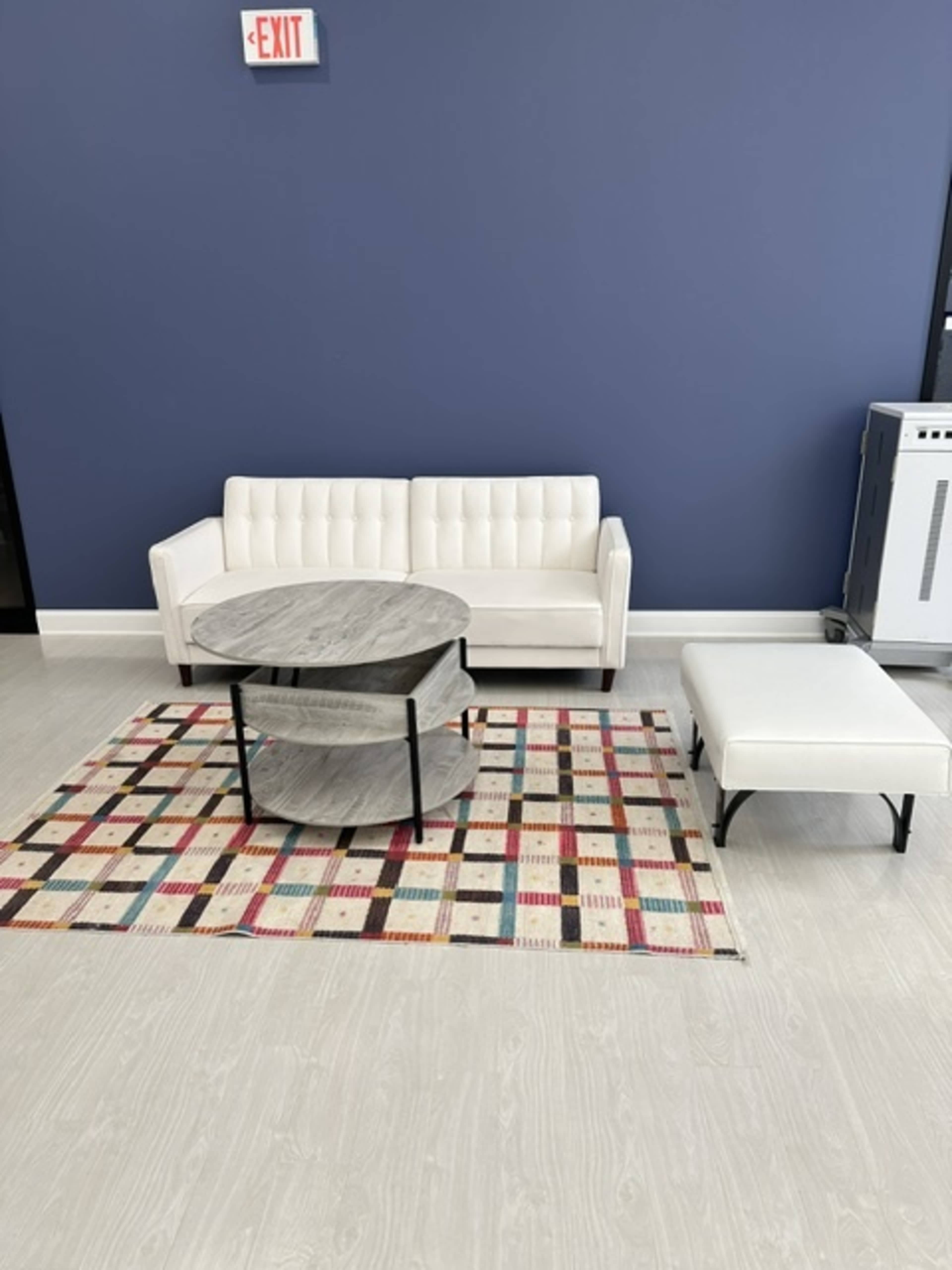 A white sofa and a round coffee table on a multicolored rug in a room with blue walls.