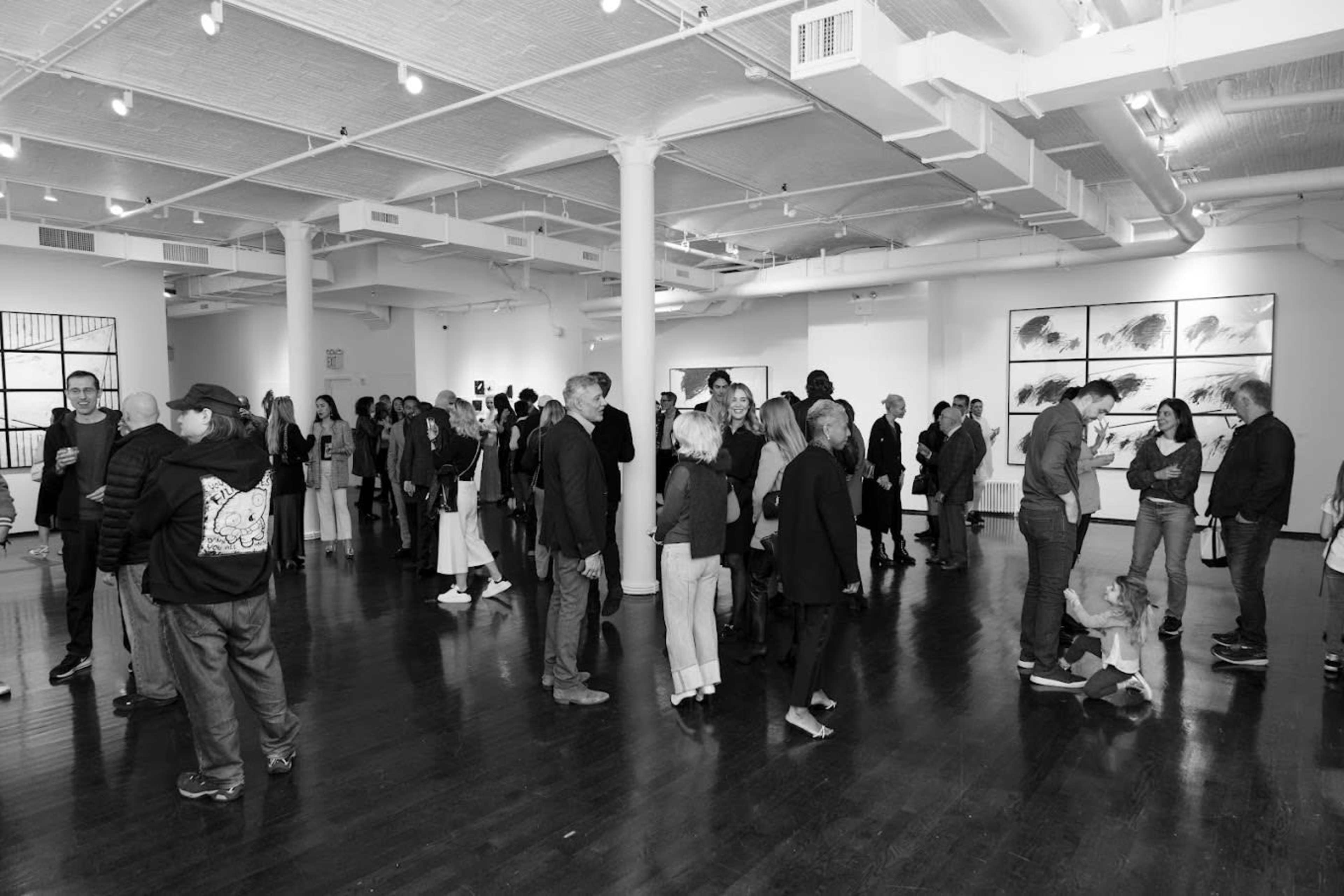 A group of people mingles in a modern art gallery featuring large framed artworks on the walls.
