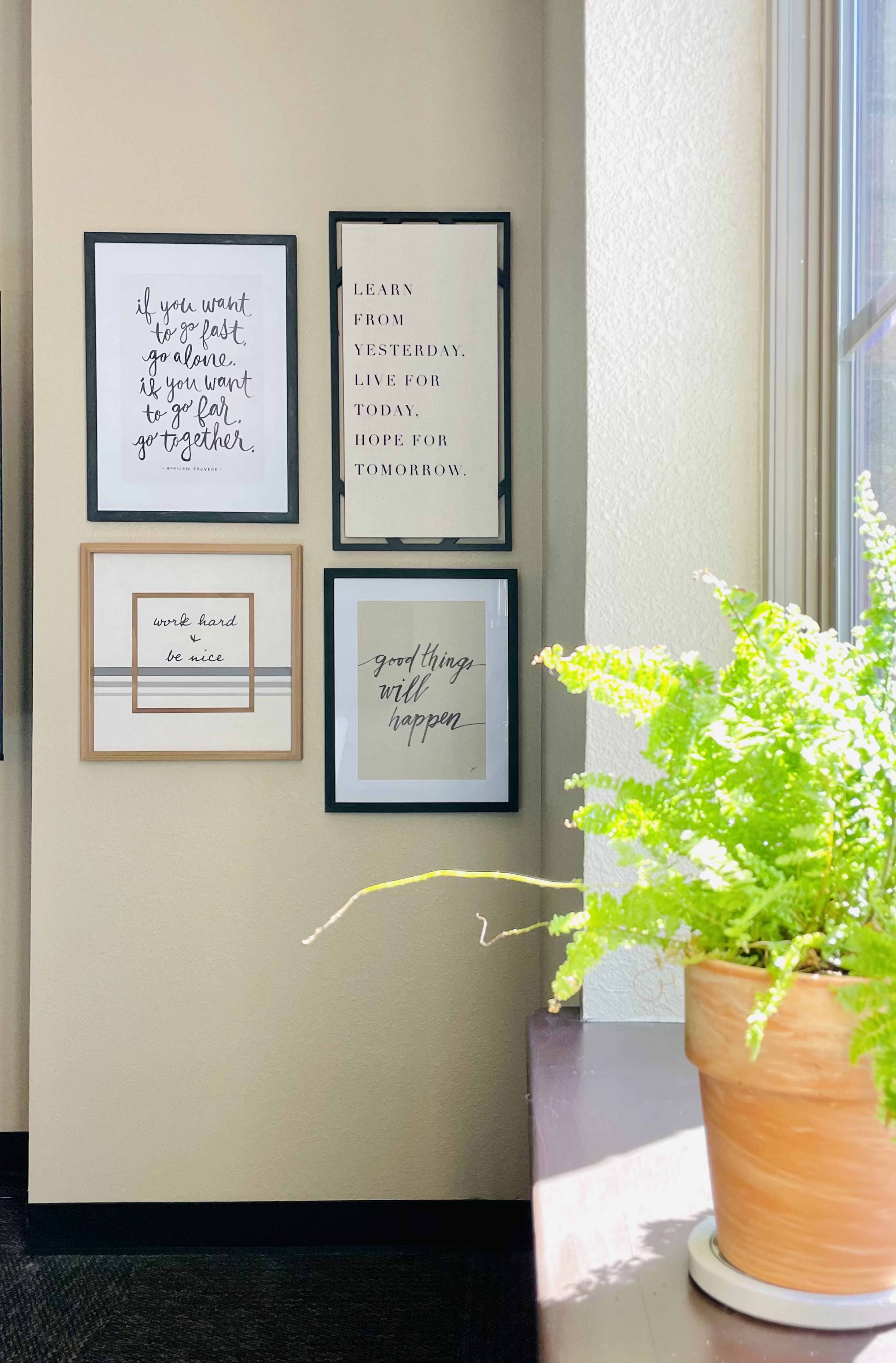 A wall with four framed motivational quotes and a potted fern on a windowsill.