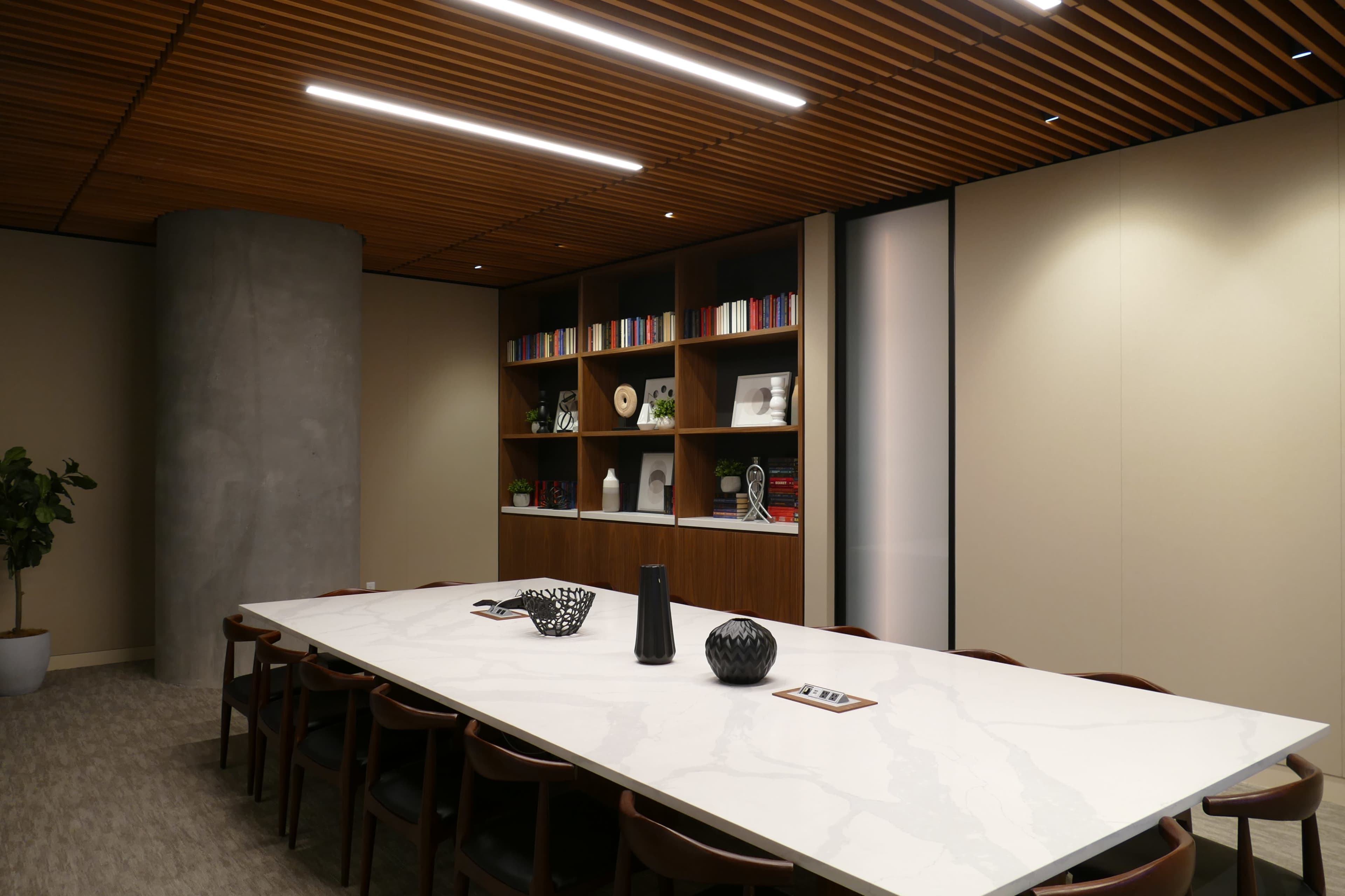 A modern conference room features a large marble table surrounded by wooden chairs, with floor-to-ceiling shelves filled with books and decorative items.