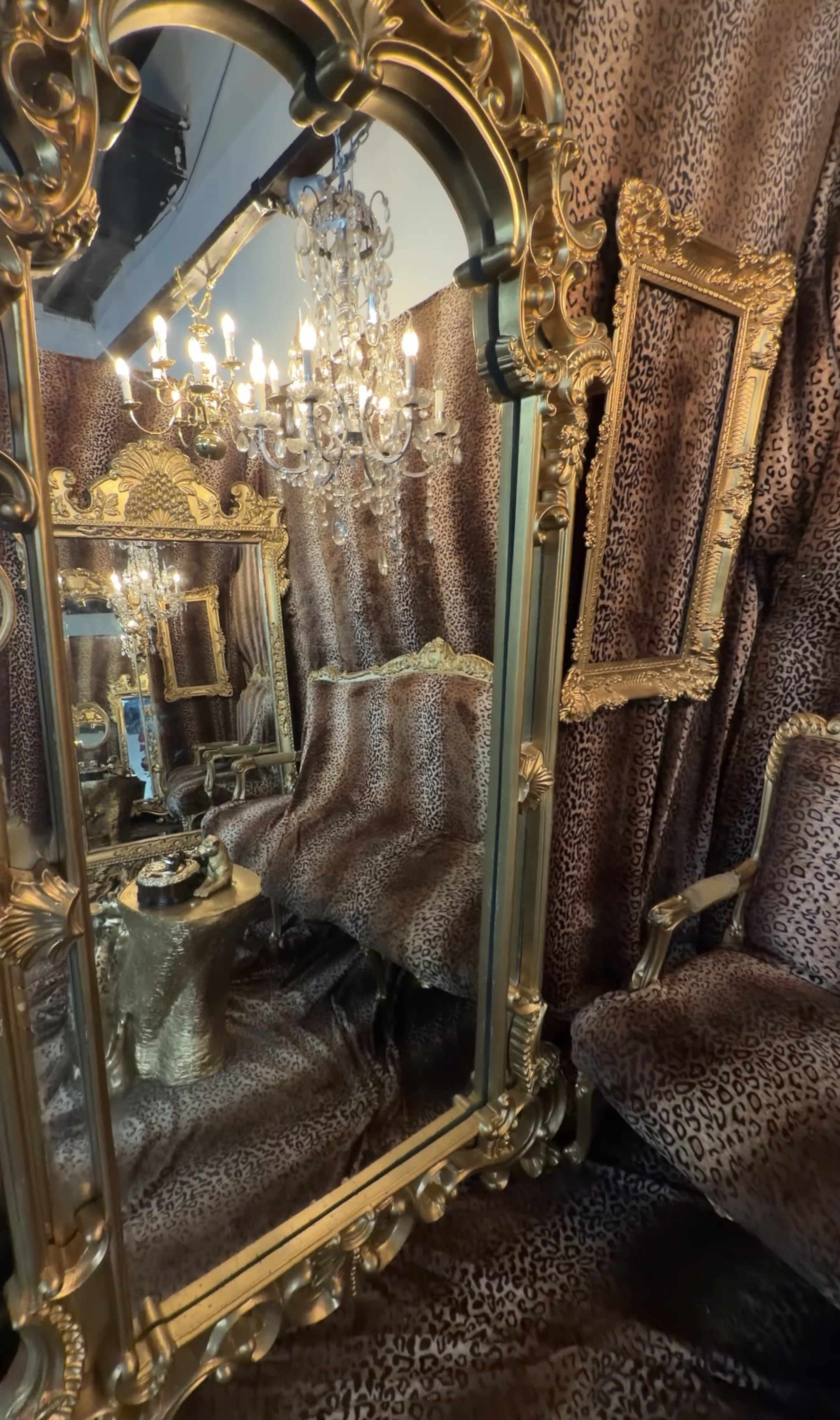 The image features an opulent room decorated with leopard-print fabric and ornate gold-framed mirrors, accented by a crystal chandelier overhead.