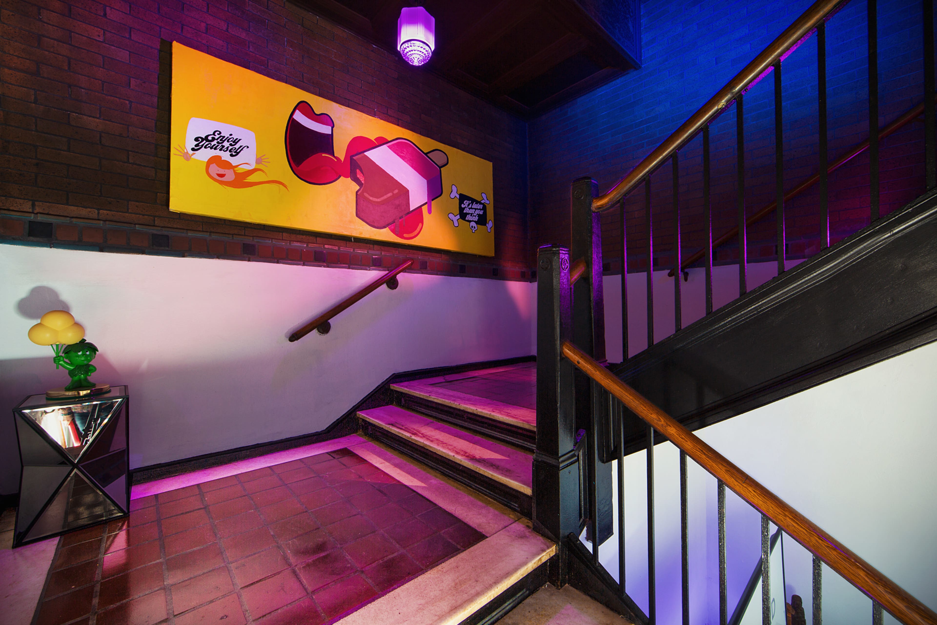 A staircase with a tiled landing features a colorful mural on the wall and a modern table with decorative items at the base.