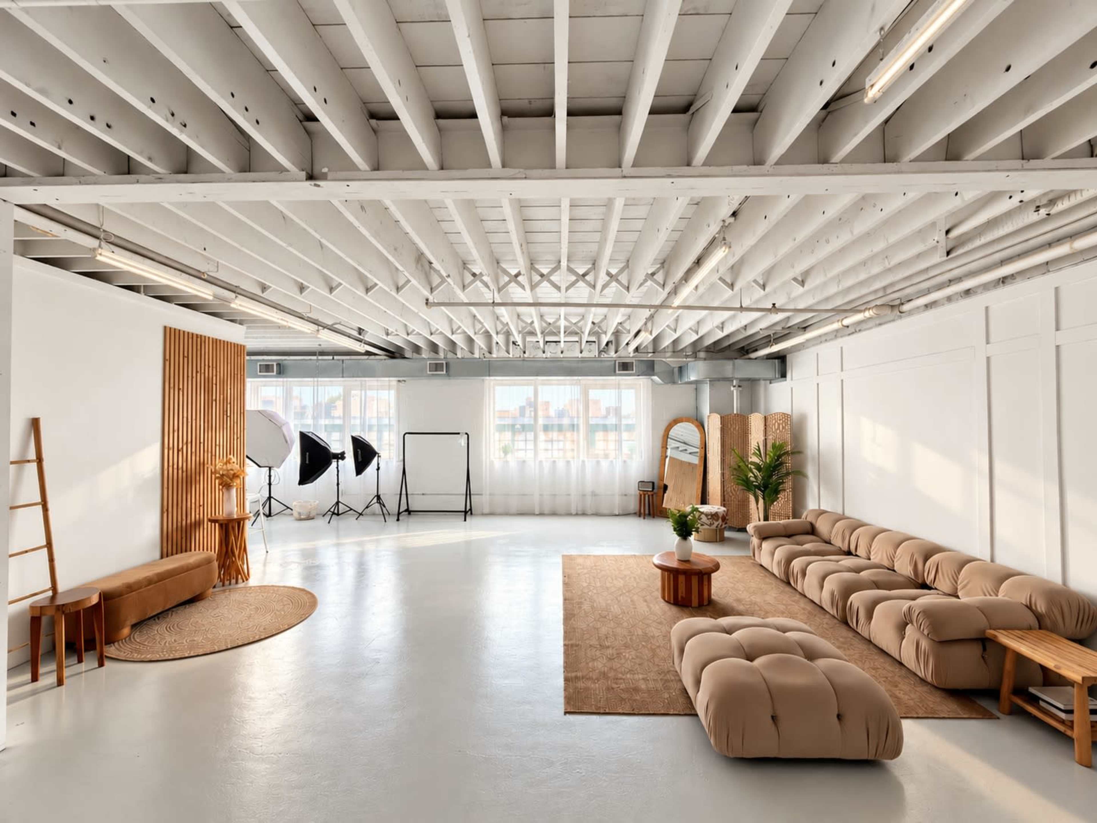 The image shows a spacious, modern interior with light-colored walls, a wooden ladder, a large sofa, and photography equipment in the background.