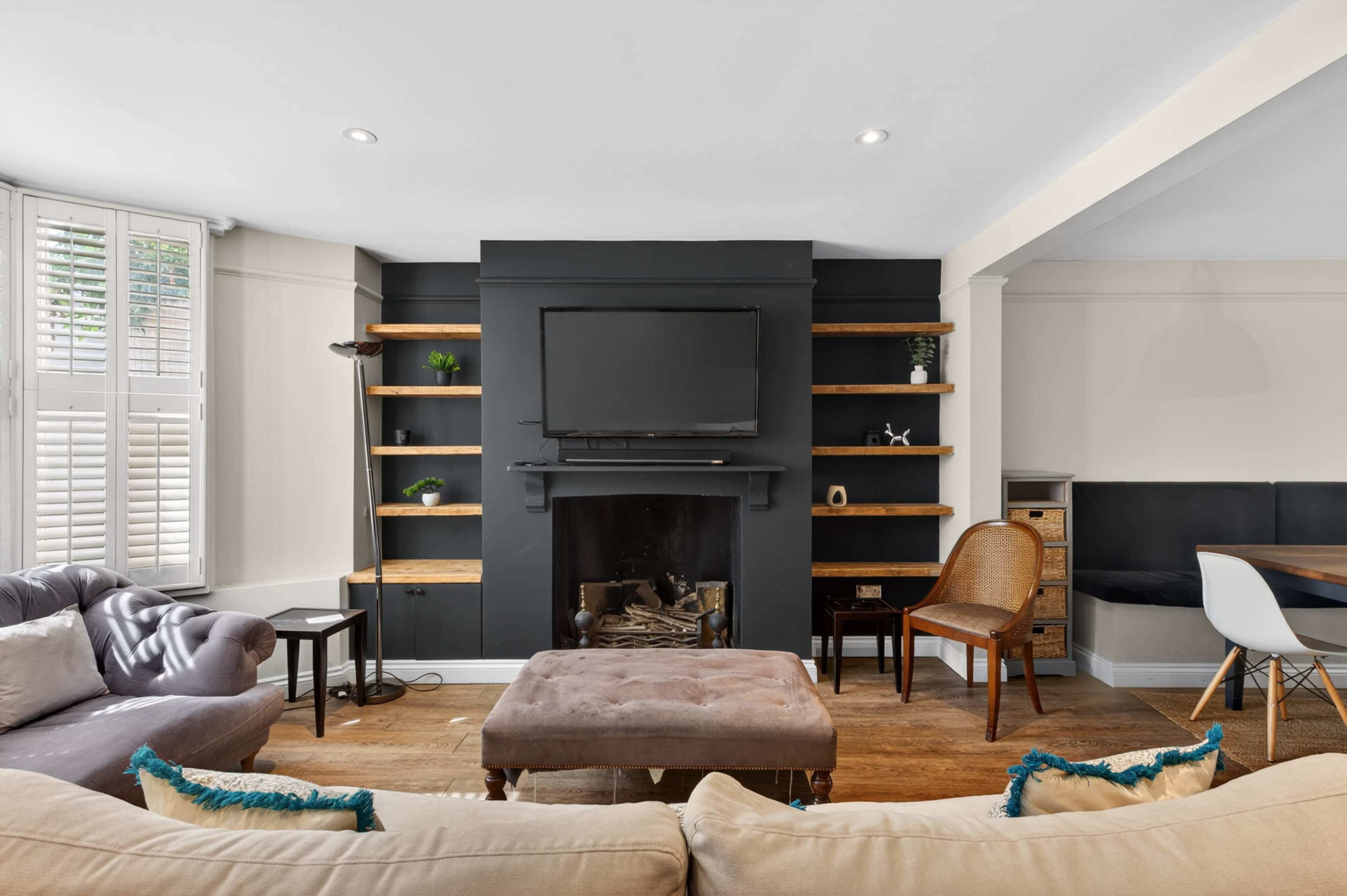 The image shows a modern living room featuring a black fireplace with built-in shelves, a television mounted above it, and a combination of light and dark furniture.