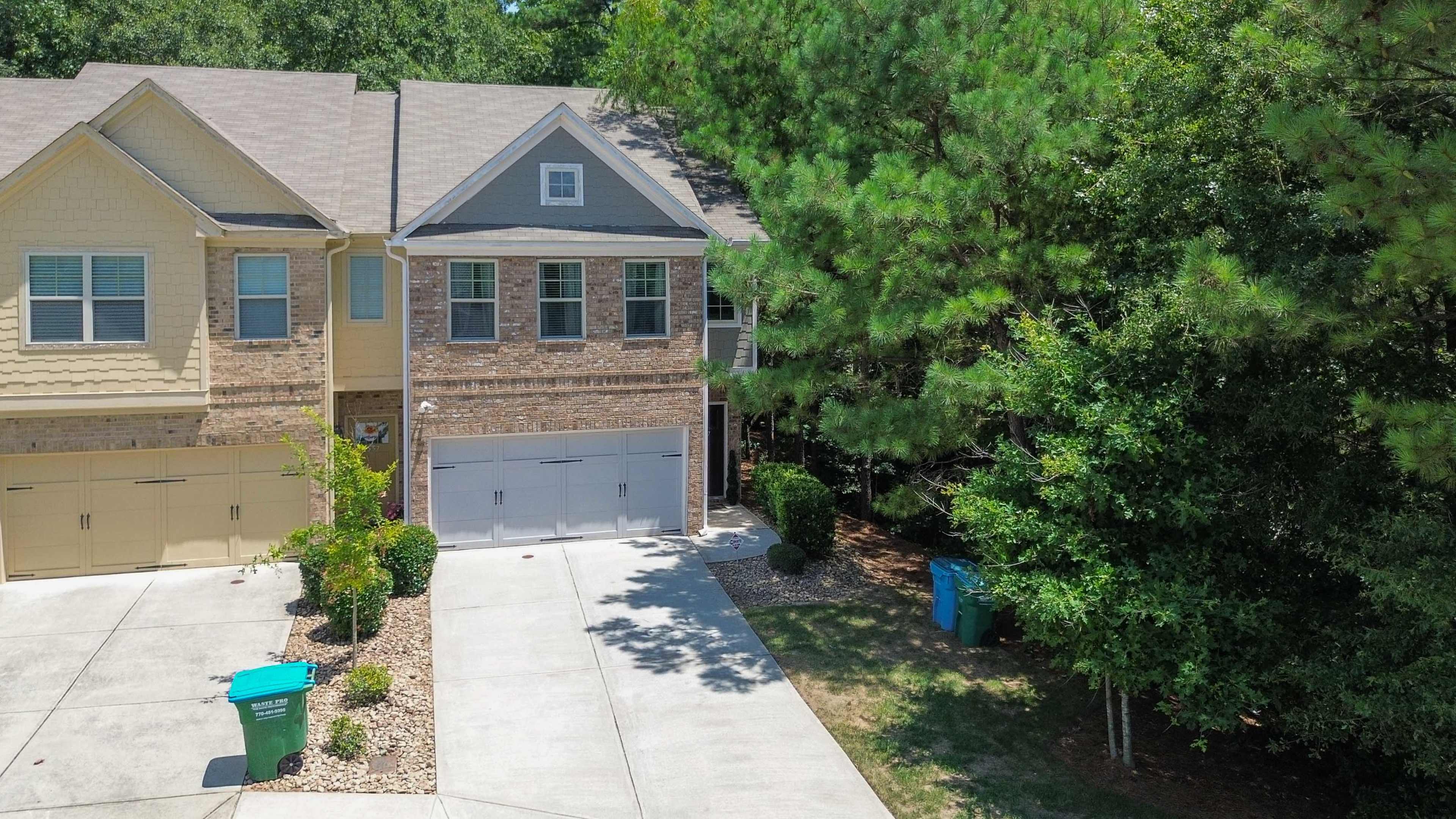 A two-story house with a brick facade and a driveway, surrounded by trees and landscaping.