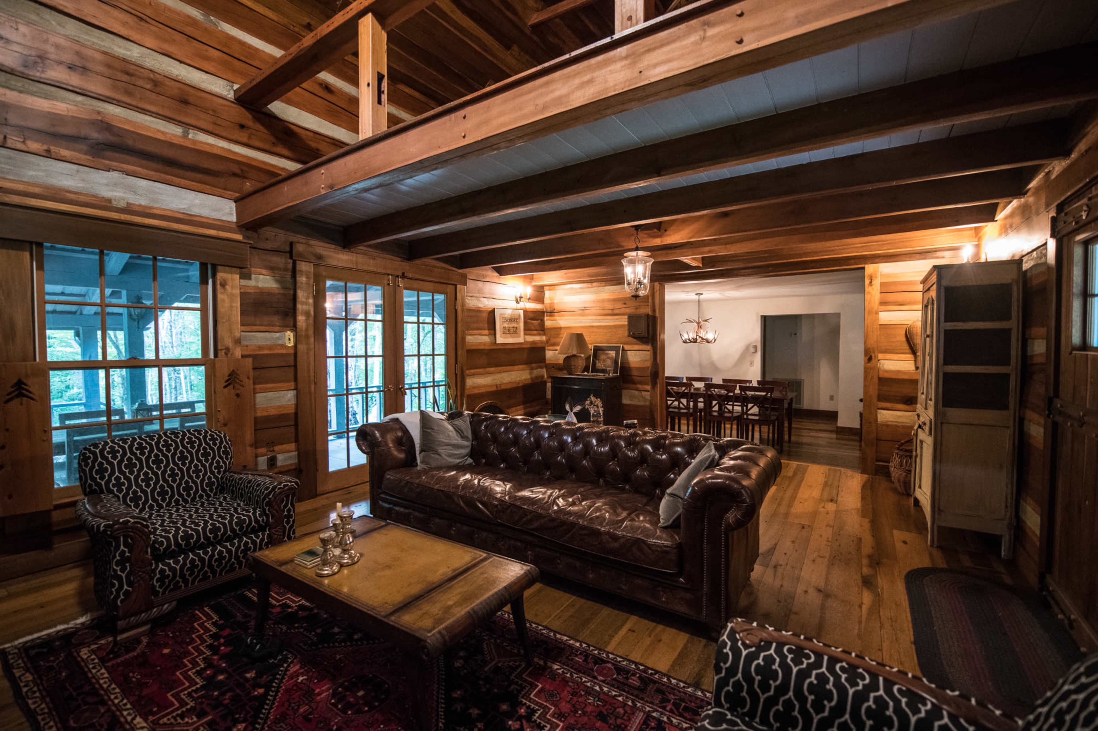 The image shows a cozy log cabin interior with a leather sofa, wooden beams, and a dining area in the background.