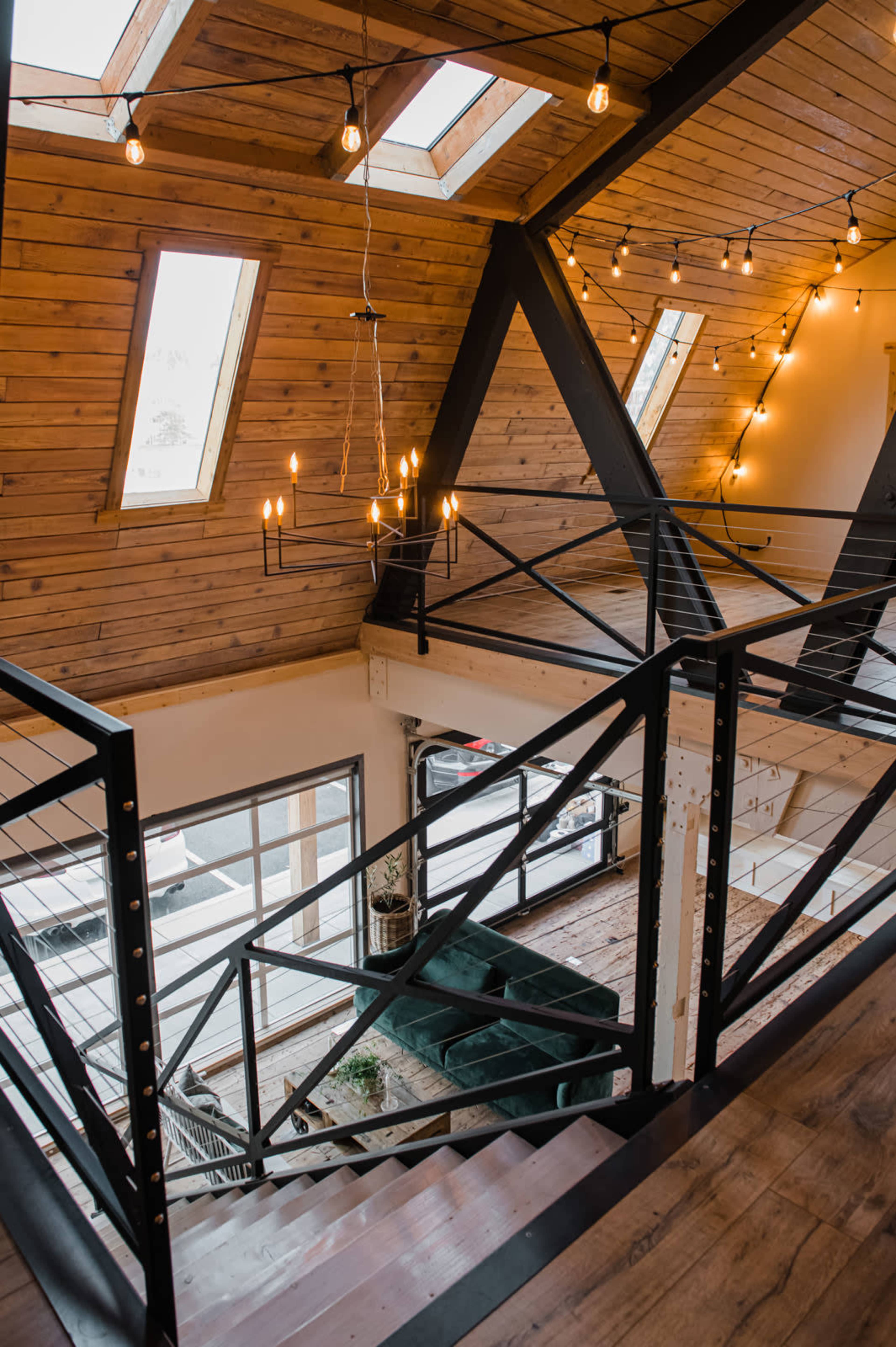 A modern two-story interior with wooden walls, large skylights, and a combination of metal and wood railings leading down a staircase to a living area below.