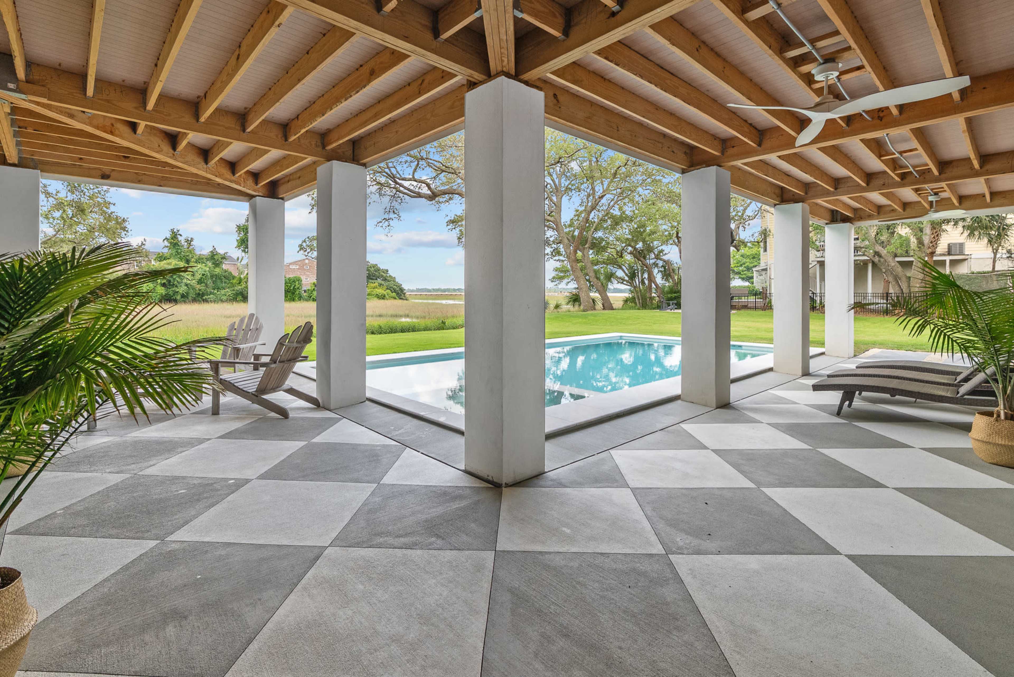 The image shows a covered patio area with a checkered floor, overlooking a pool and greenery.