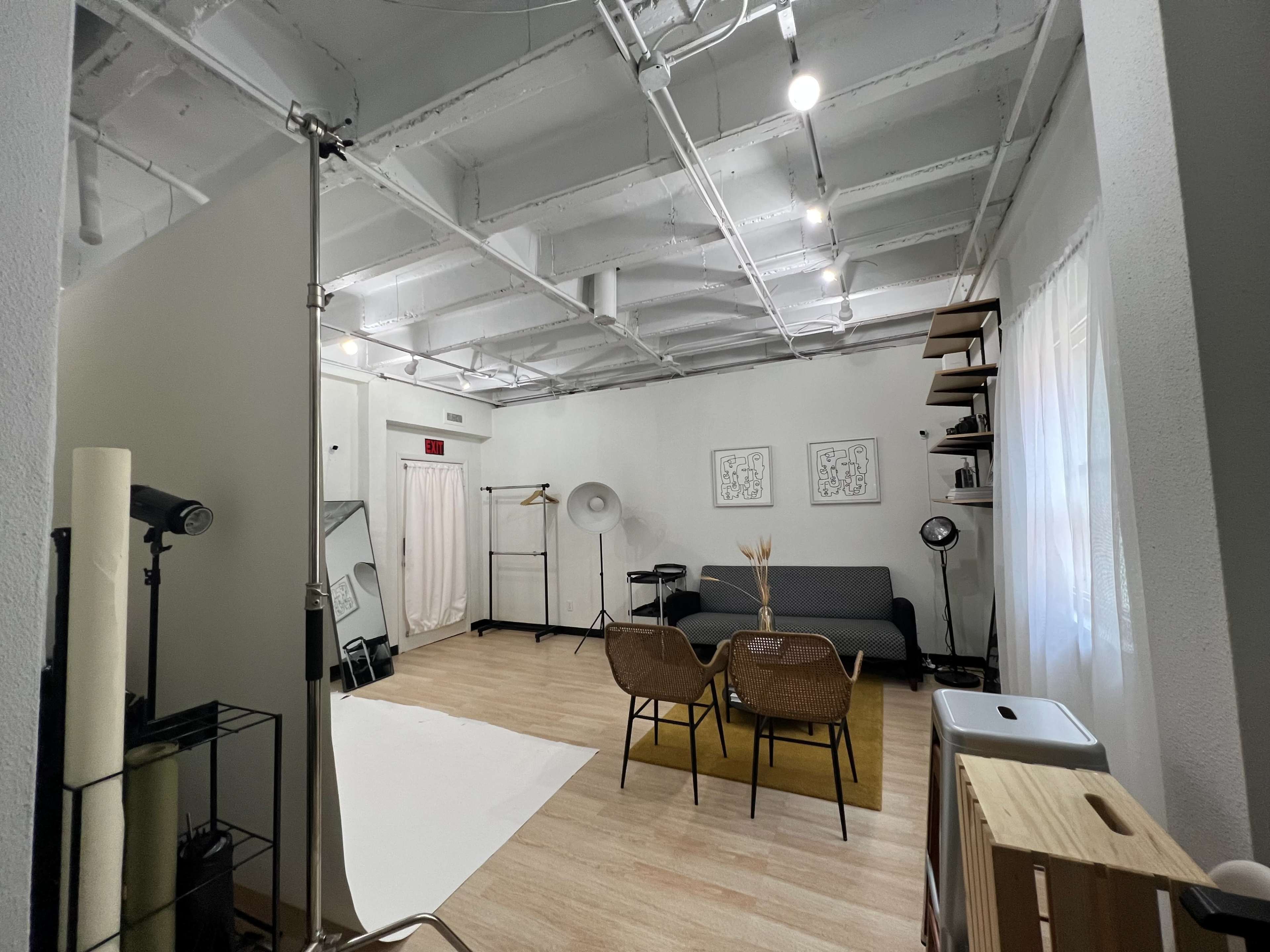 A spacious photo studio with a white backdrop, seating area, and various lighting equipment arranged around the room.