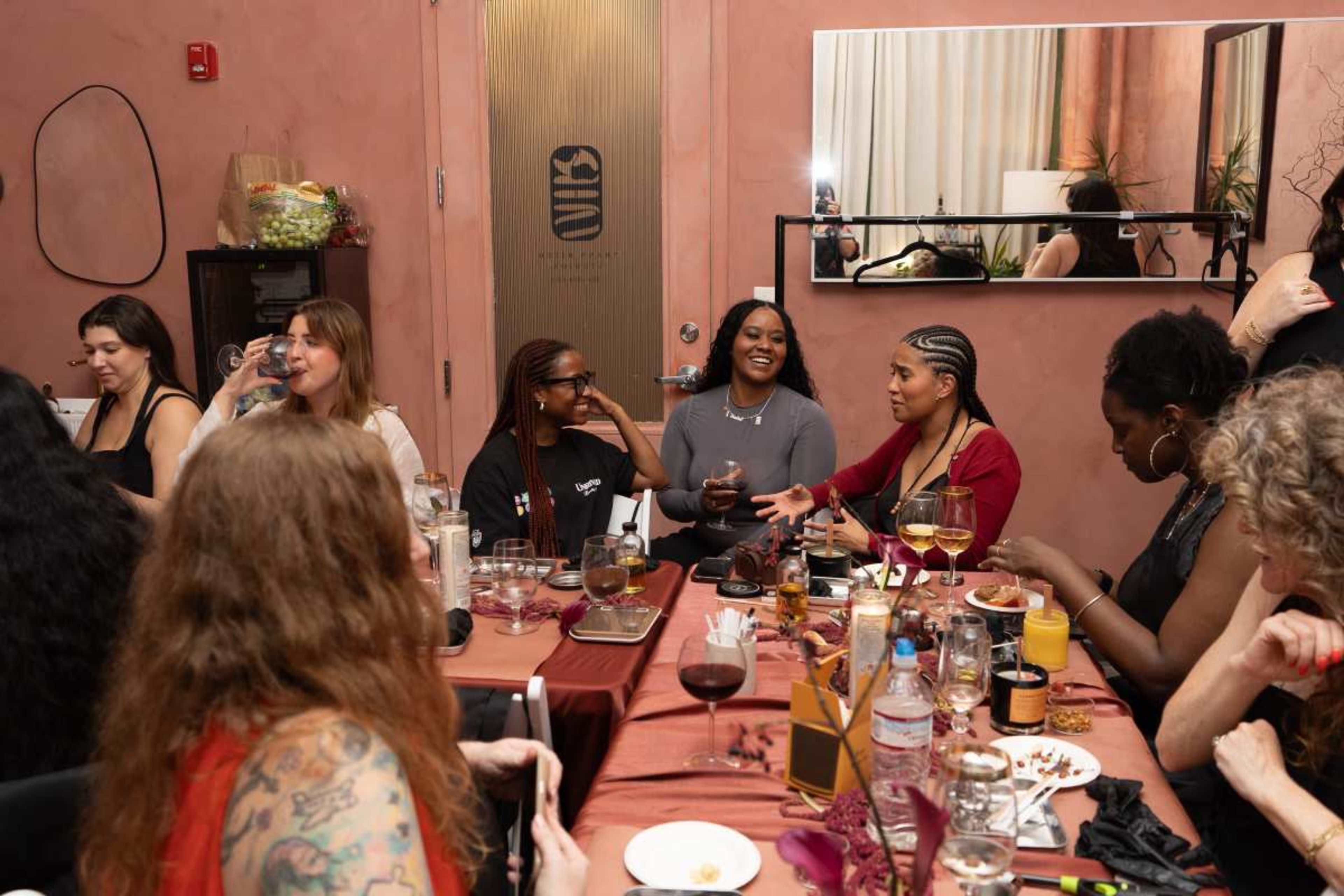 A group of people is gathered around a dining table, engaged in conversation and enjoying drinks in a warmly decorated setting.