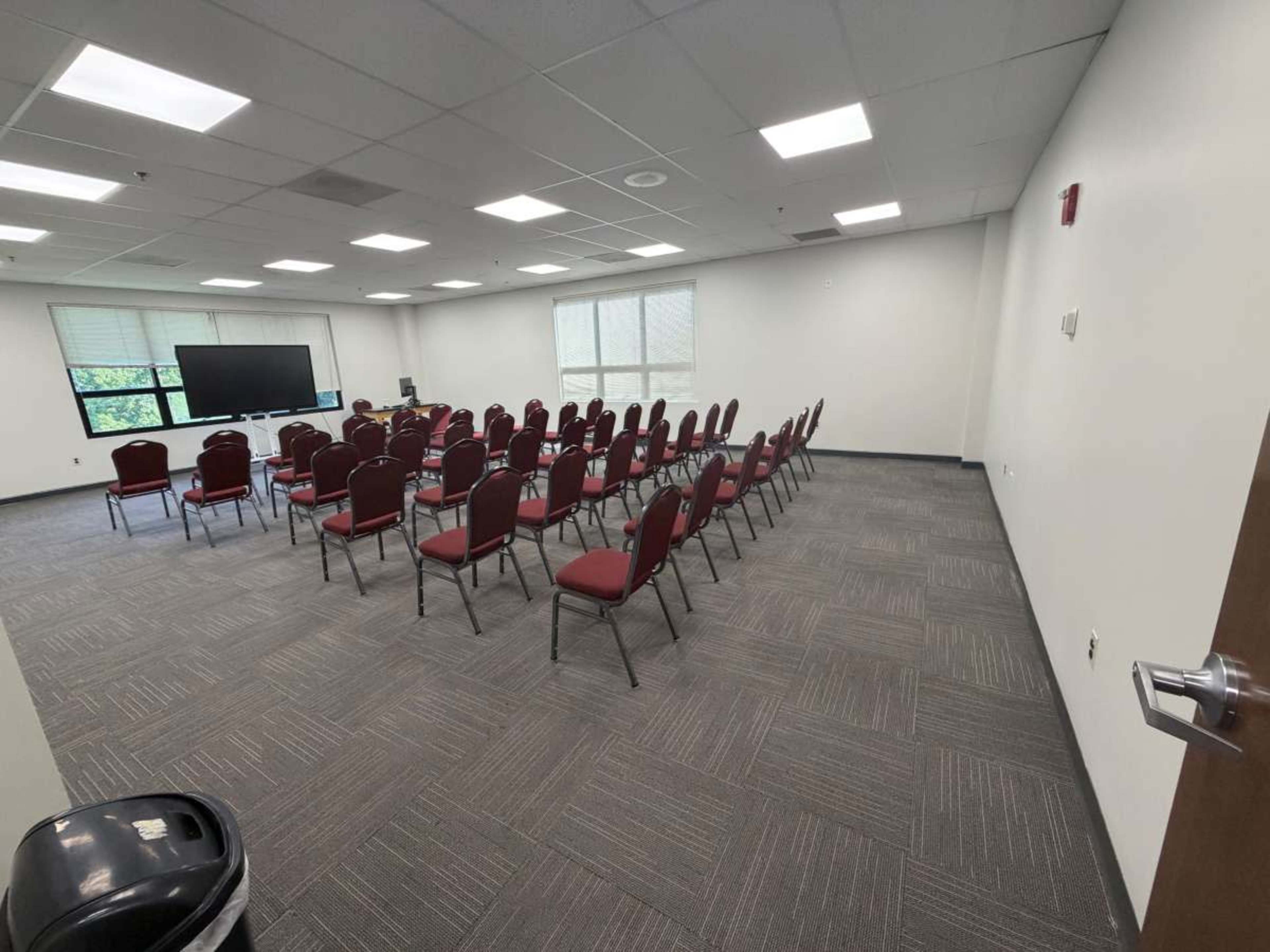 A conference room is set up with rows of red chairs facing a large screen.