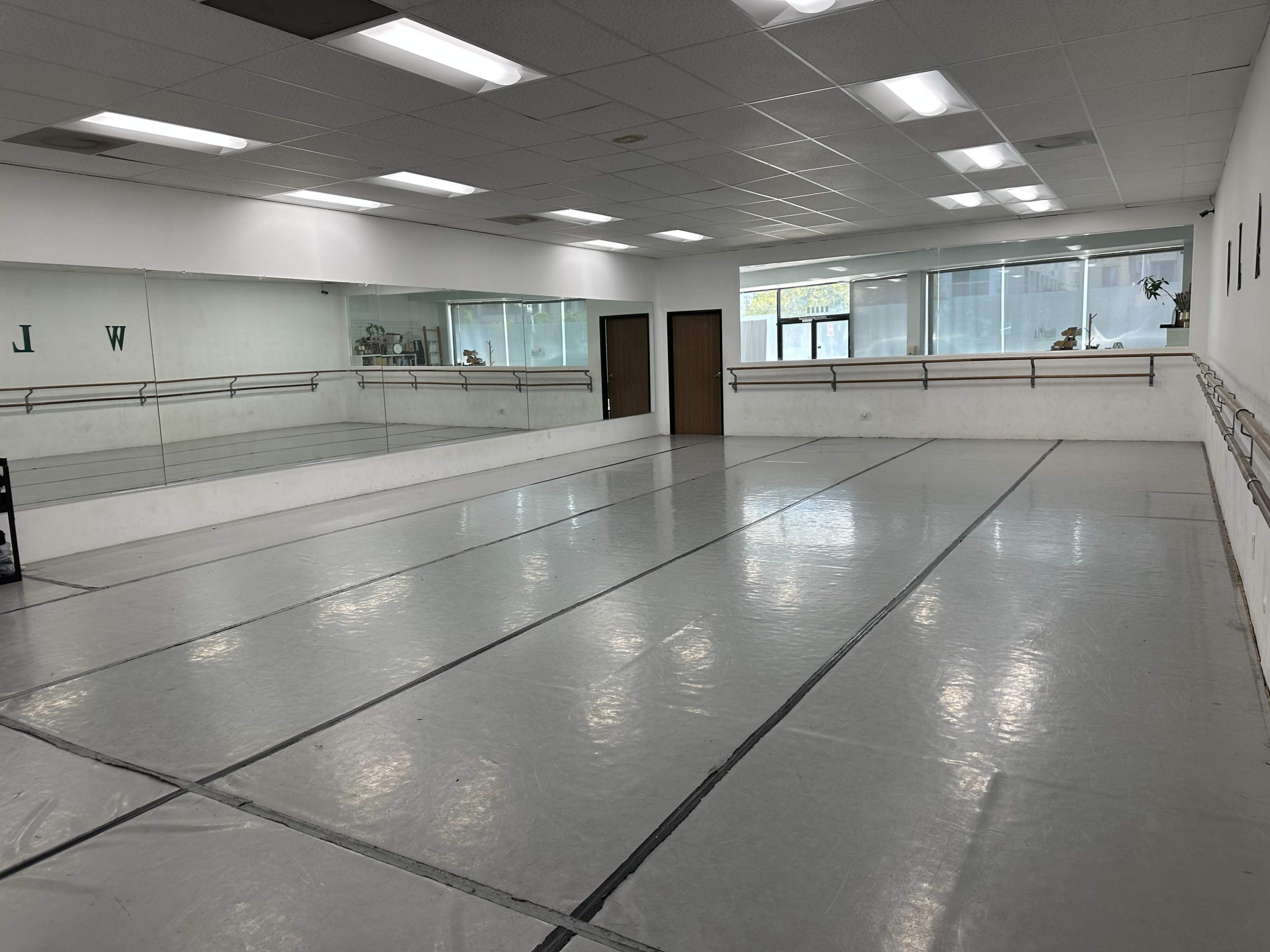 The image shows a spacious dance studio with a mirrored wall, ballet bars, and a polished floor.