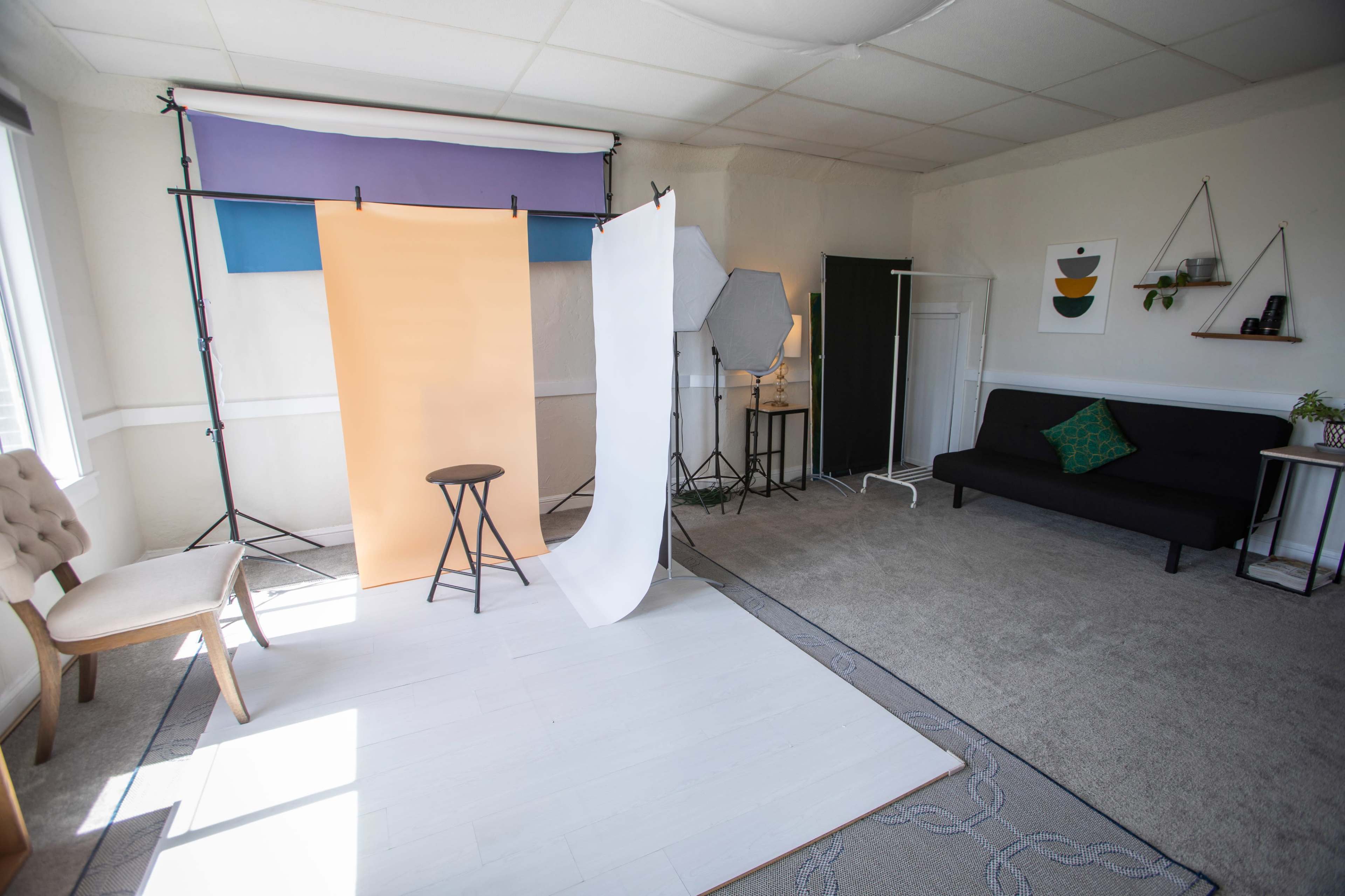A well-lit studio space featuring several backdrops, a stool, a black couch, and decorative elements on the walls.