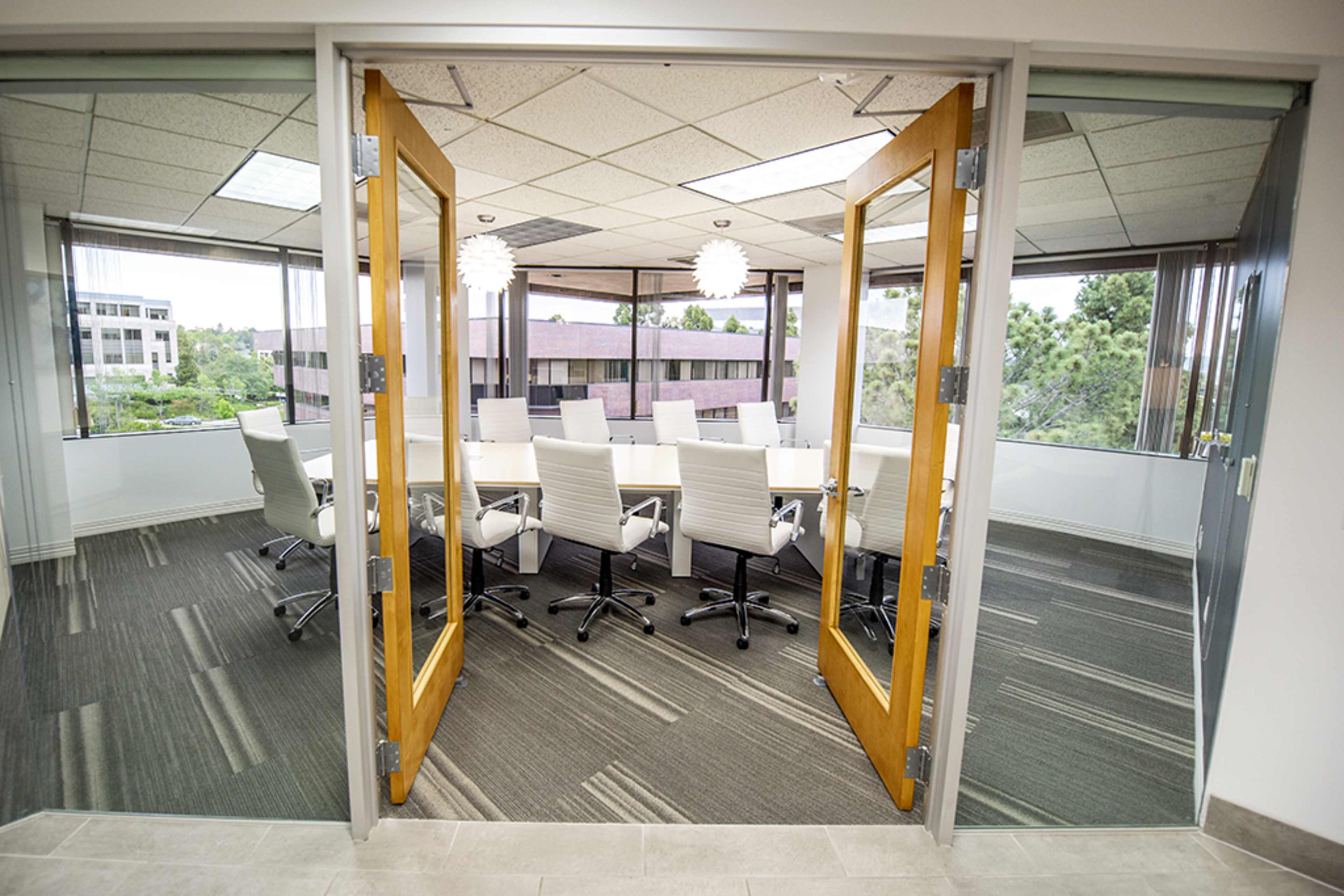 A conference room with a large table surrounded by white chairs is visible through open double doors.