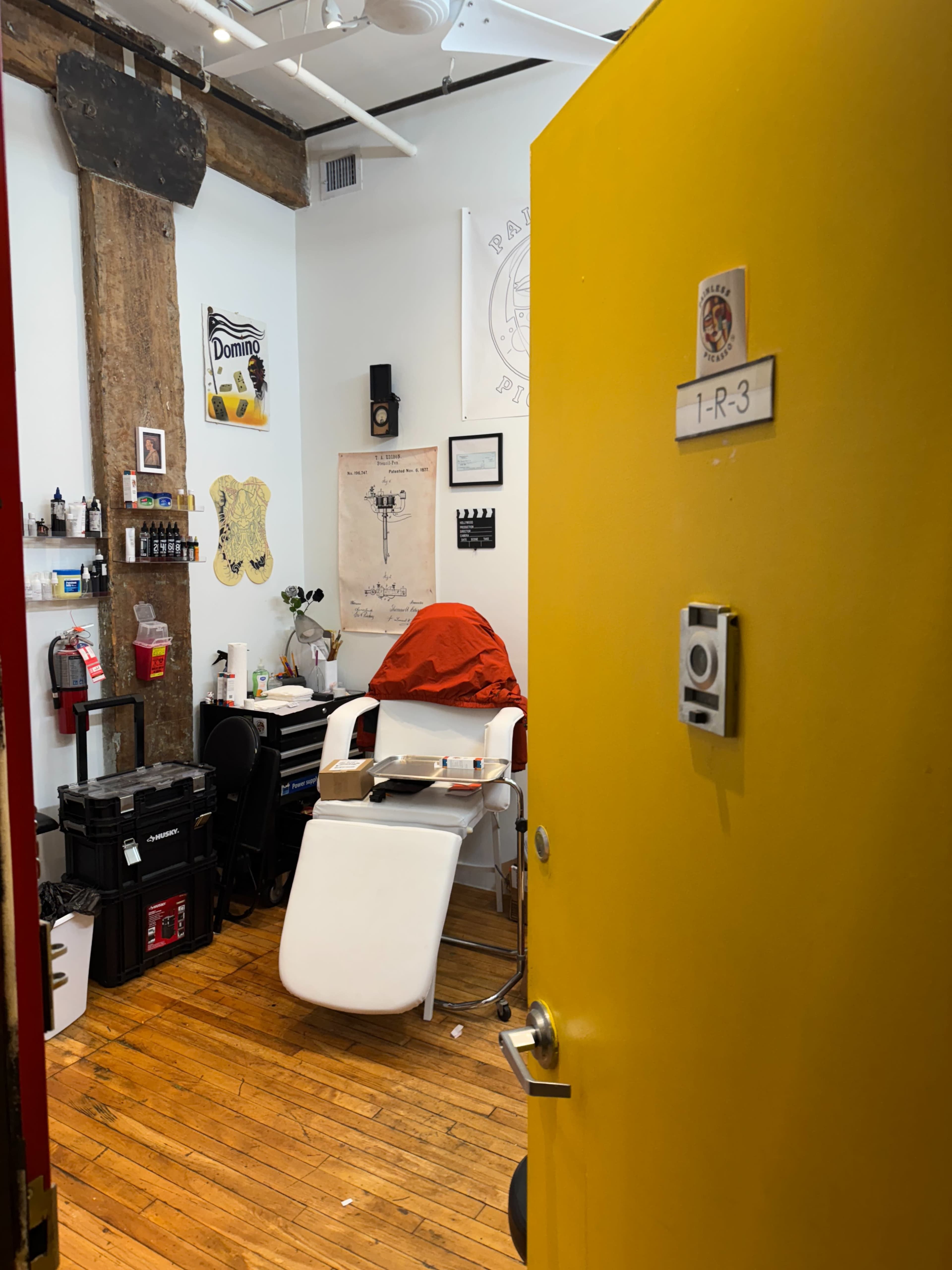 A brightly colored yellow door opens into a small hair salon featuring a barber chair, various tools, and wall decorations.