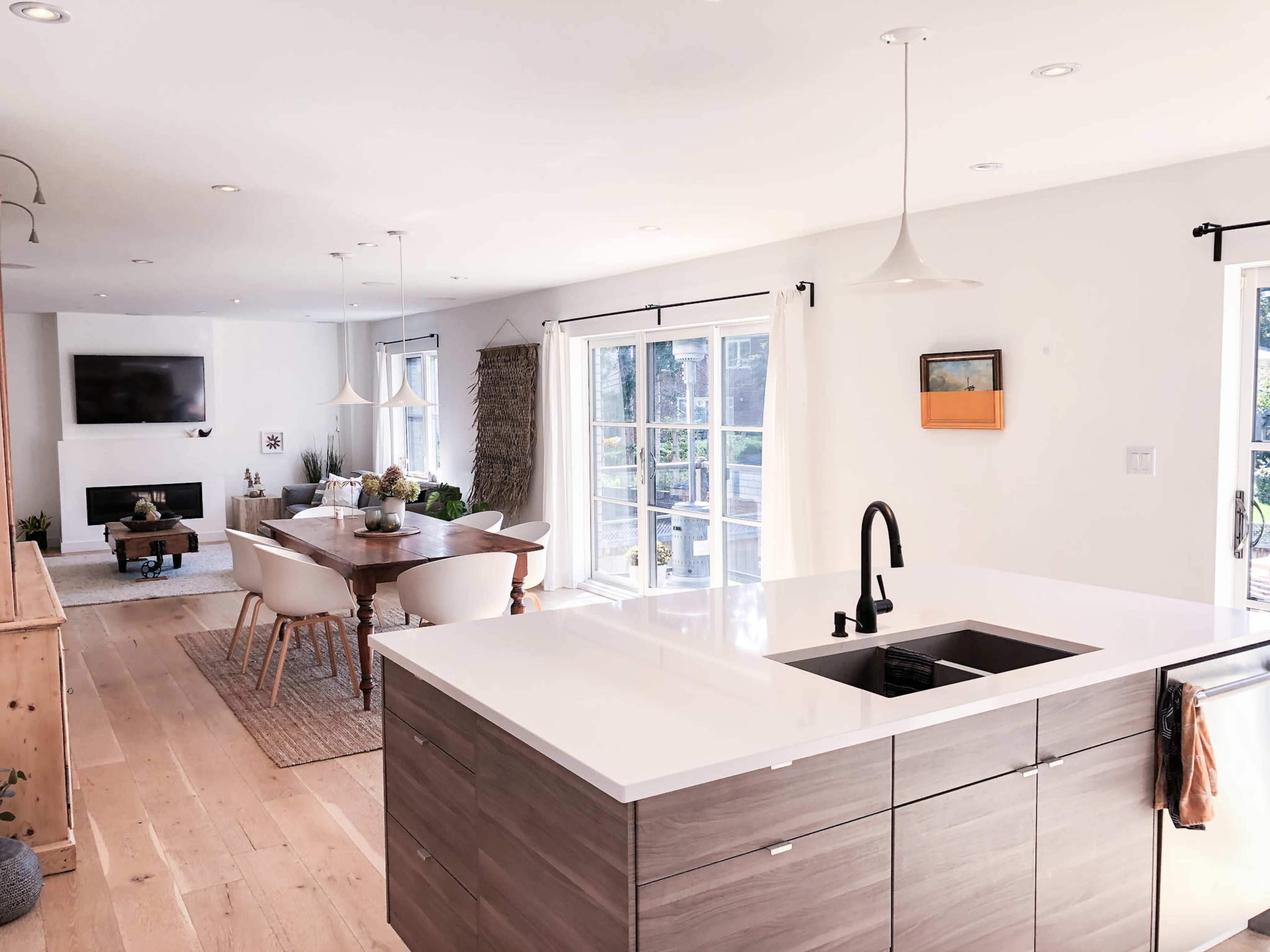 A modern kitchen with a large white countertop overlooks a dining area and living room filled with natural light.