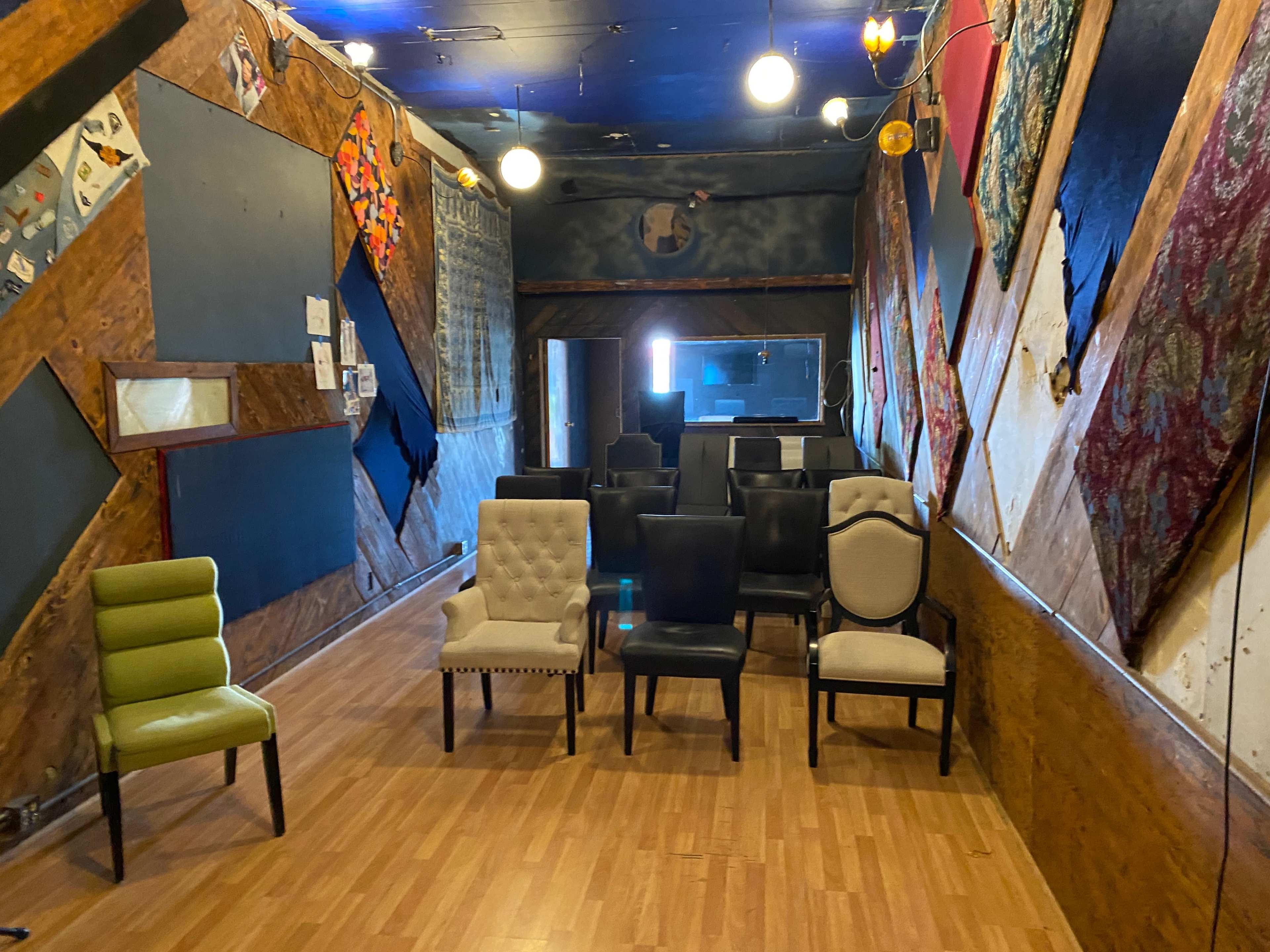 A room with various chairs arranged in a semi-circle facing a wall, with an eclectic design of wood and fabric decorations on the walls.