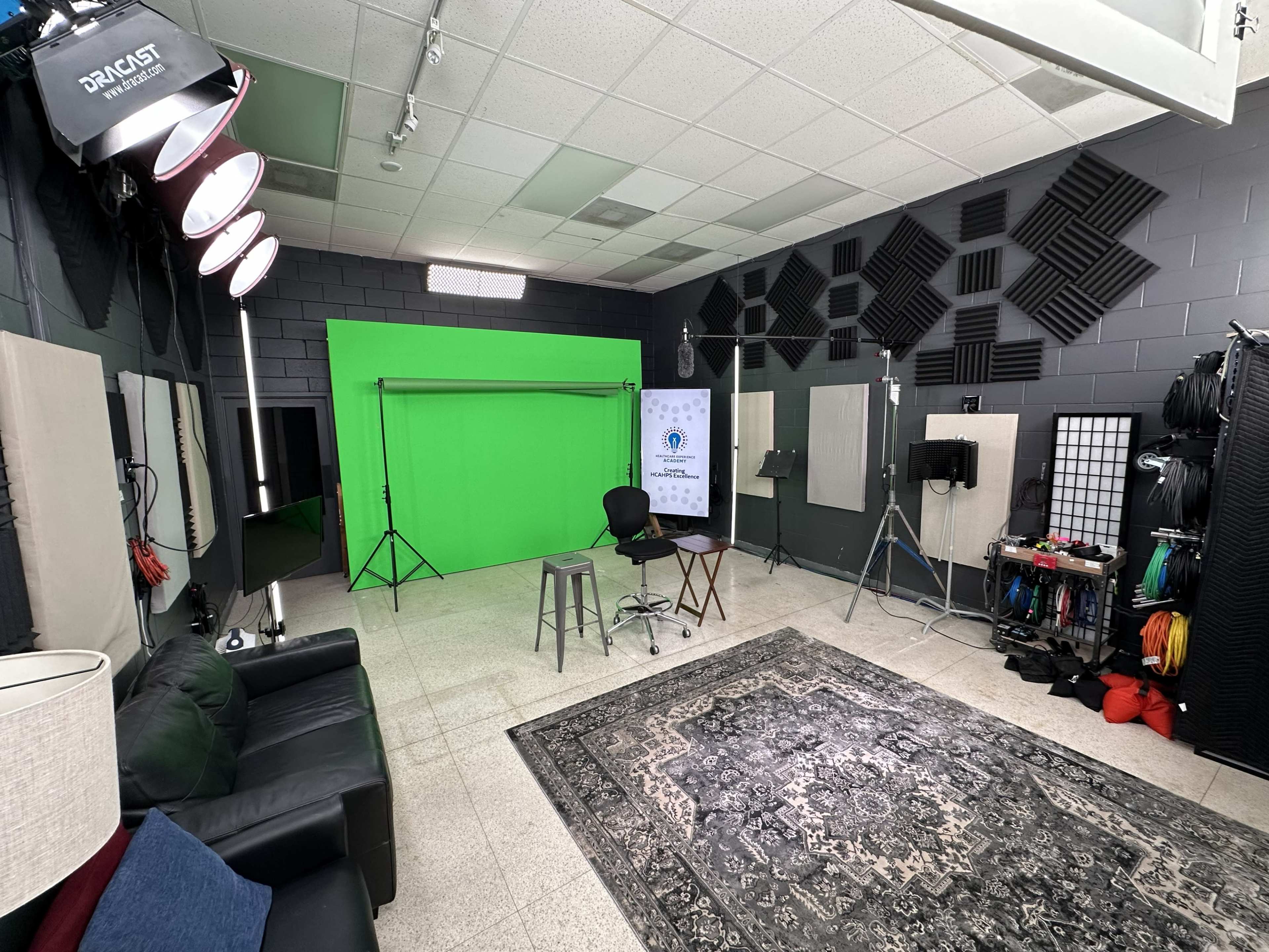 The image shows a studio space with a green screen, lighting equipment, and various film accessories arranged around the room.
