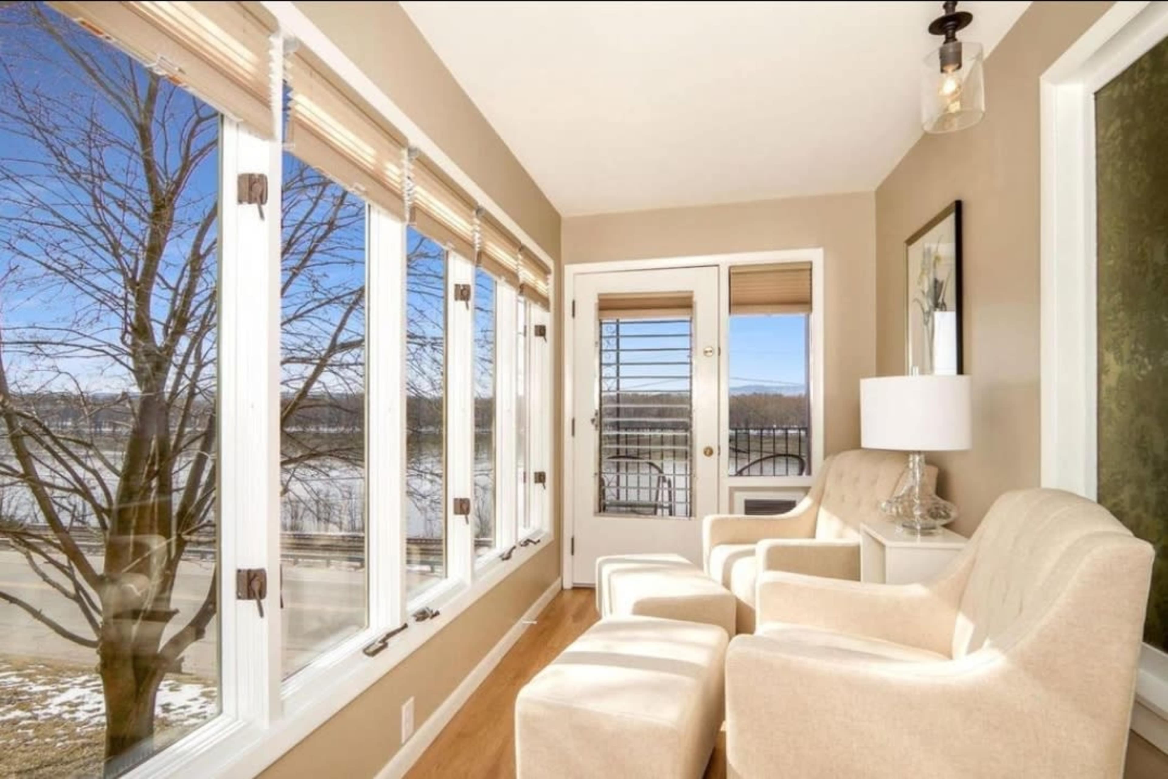 A bright room features two chairs positioned by large windows overlooking a river and a tree outside.