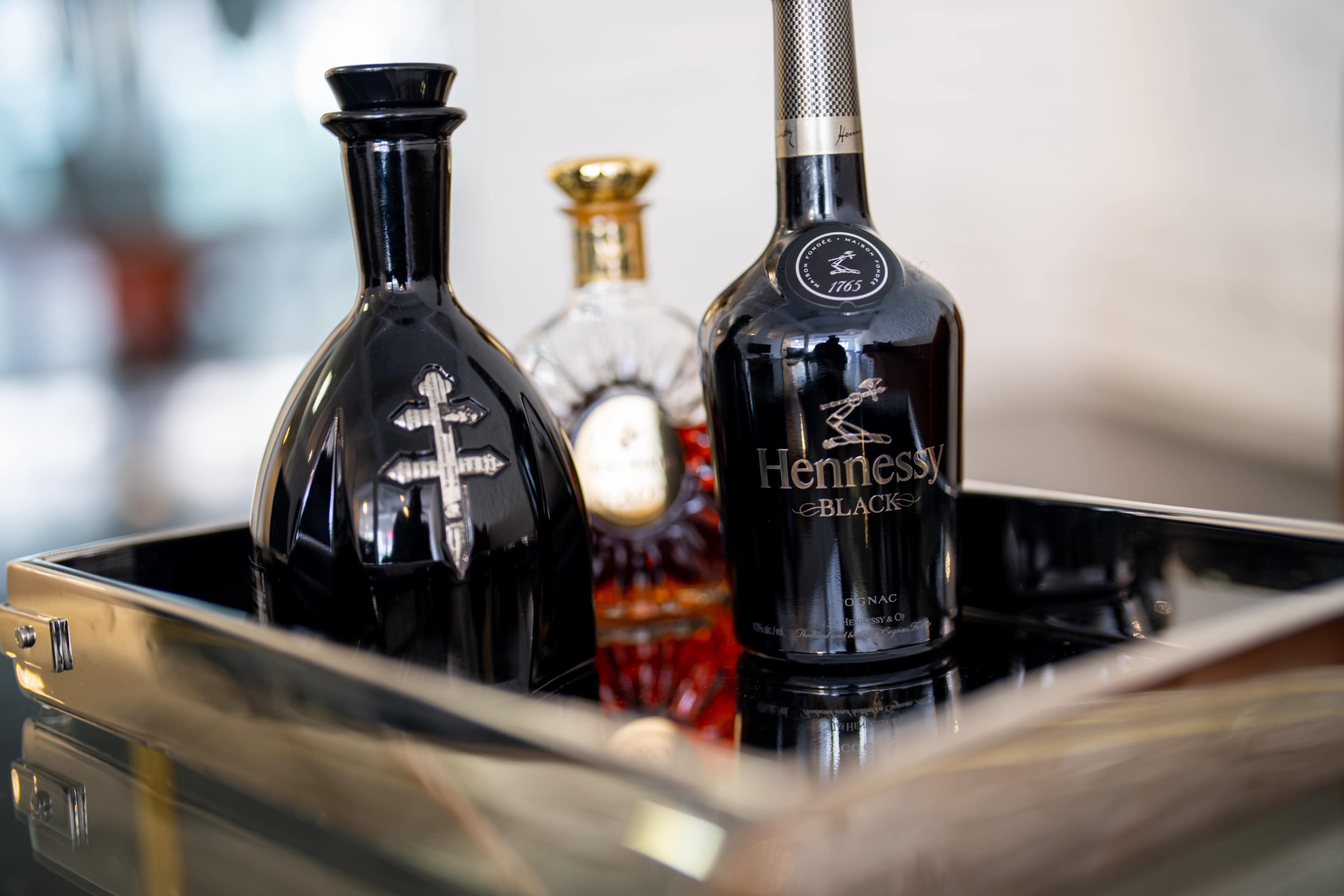 Three bottles of liquor, including Hennessy Black, are arranged on a reflective tray.