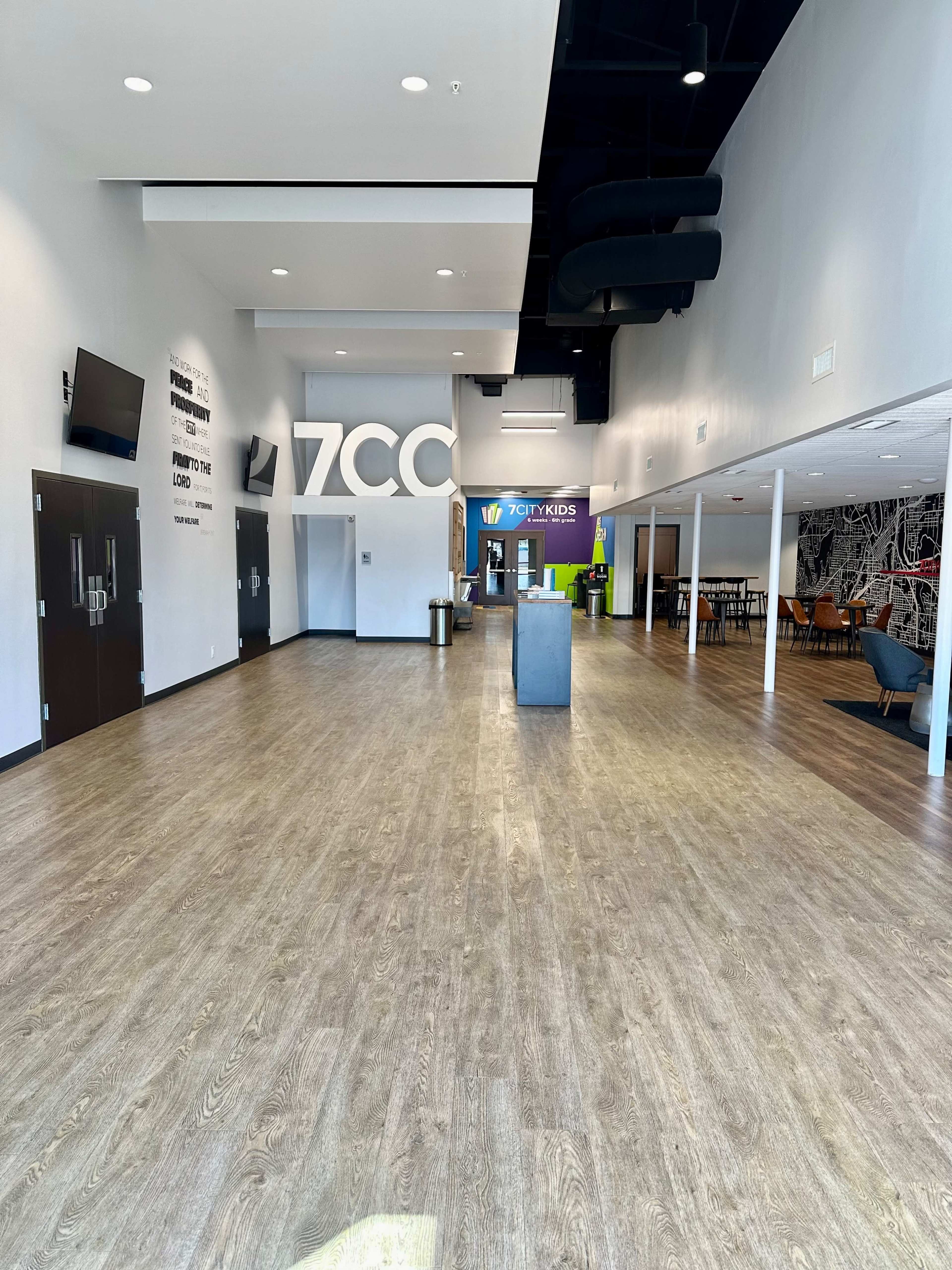 The image shows a spacious, modern interior of a building with a large entrance area, wooden floors, and various rooms visible in the background.