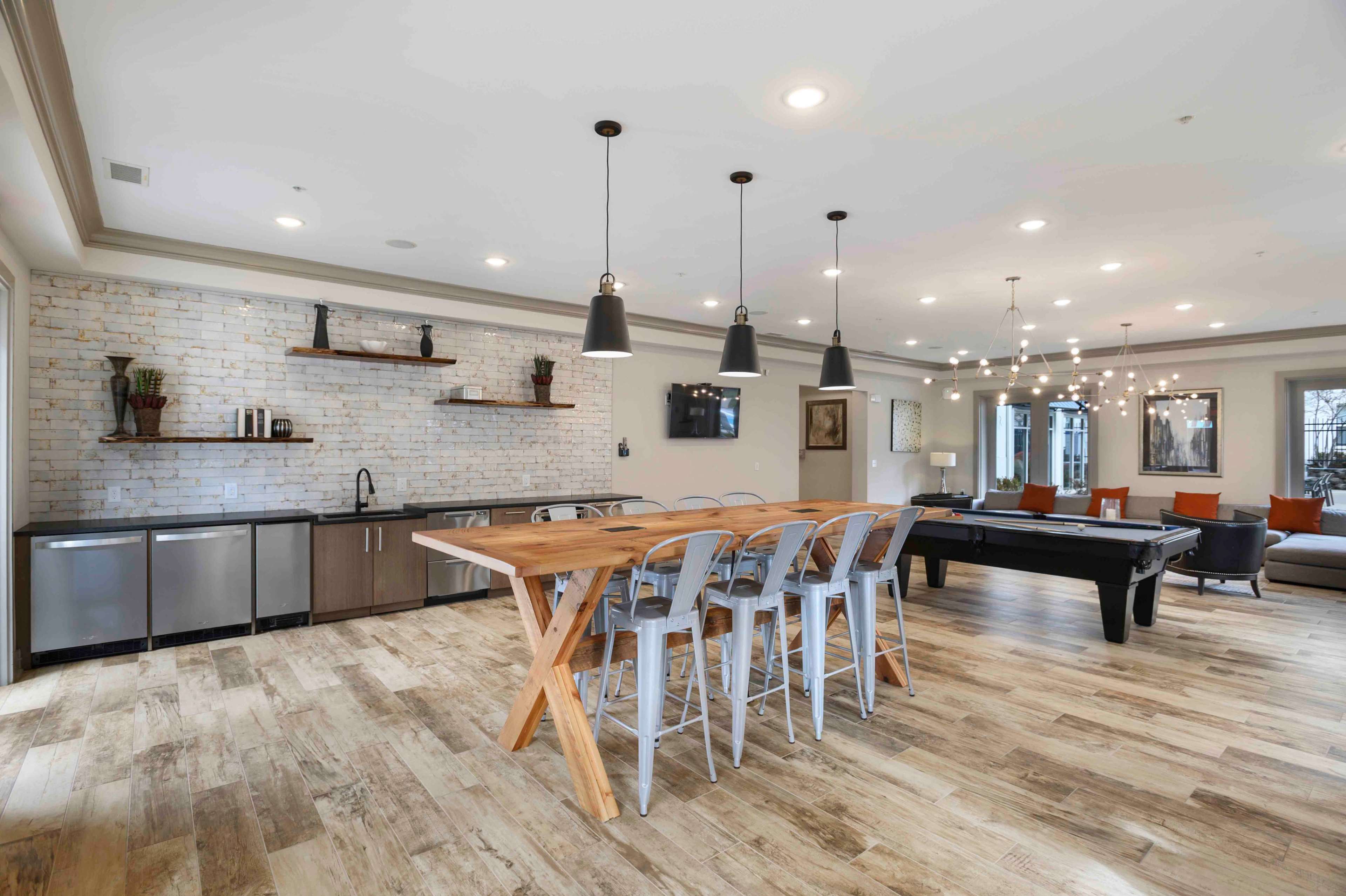 A modern, open-concept room featuring a dining table with metal chairs, a kitchenette with appliances, and a pool table.