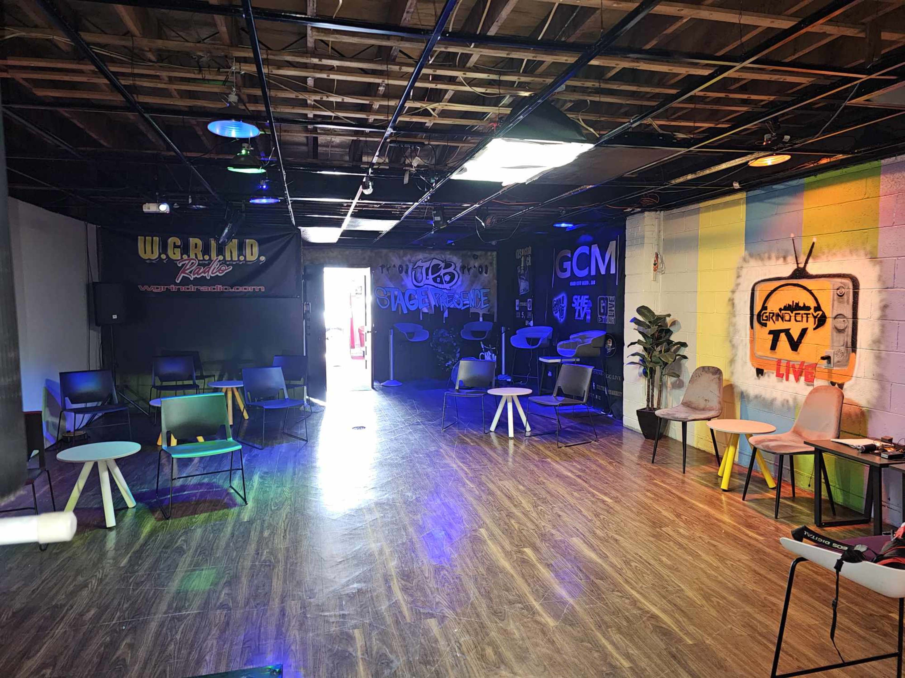 A spacious room with modern chairs and tables, featuring colorful murals and various lighting setups.