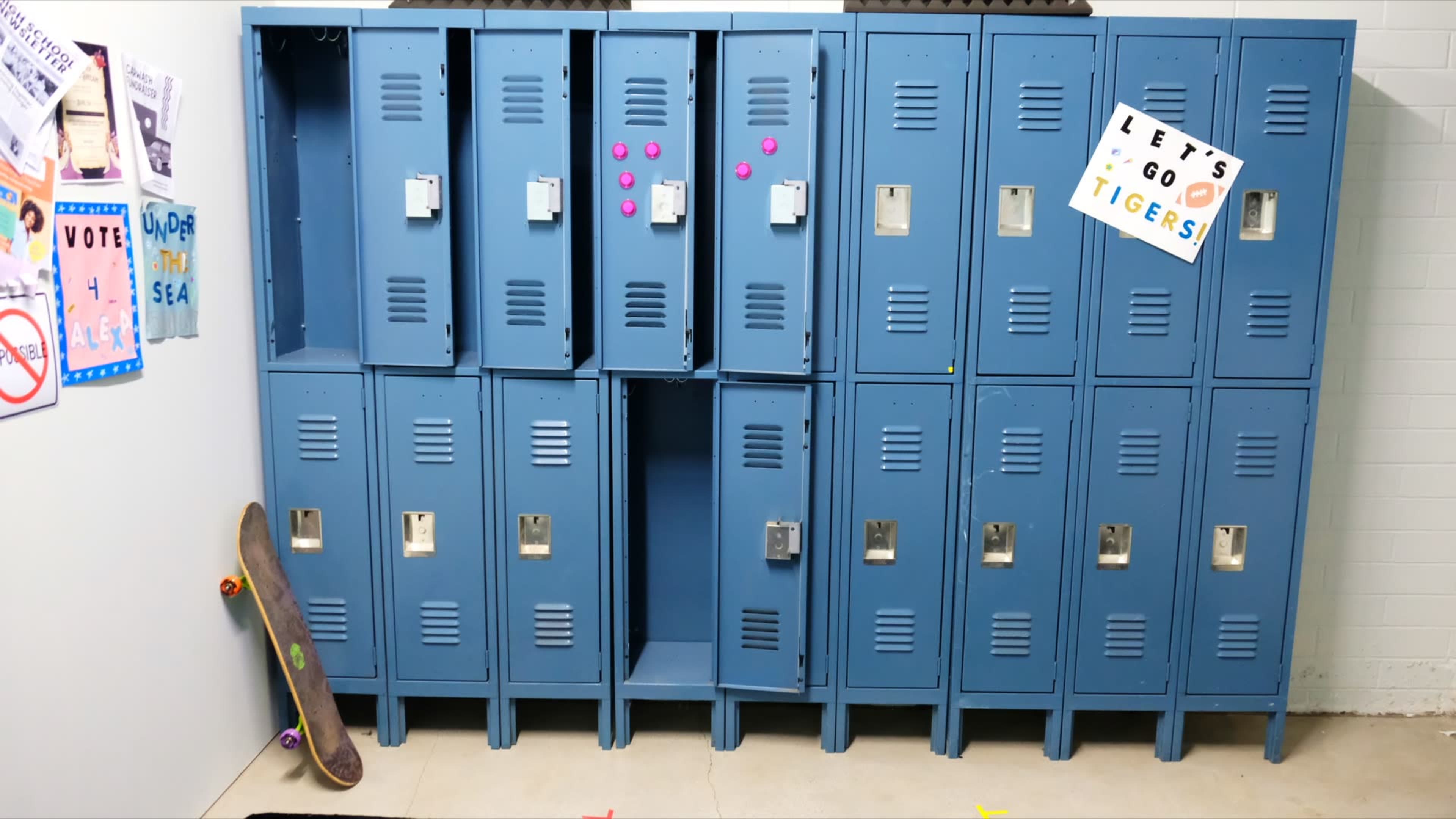 The image shows a row of blue school lockers, with one locker open, and a skateboard resting against the wall nearby.