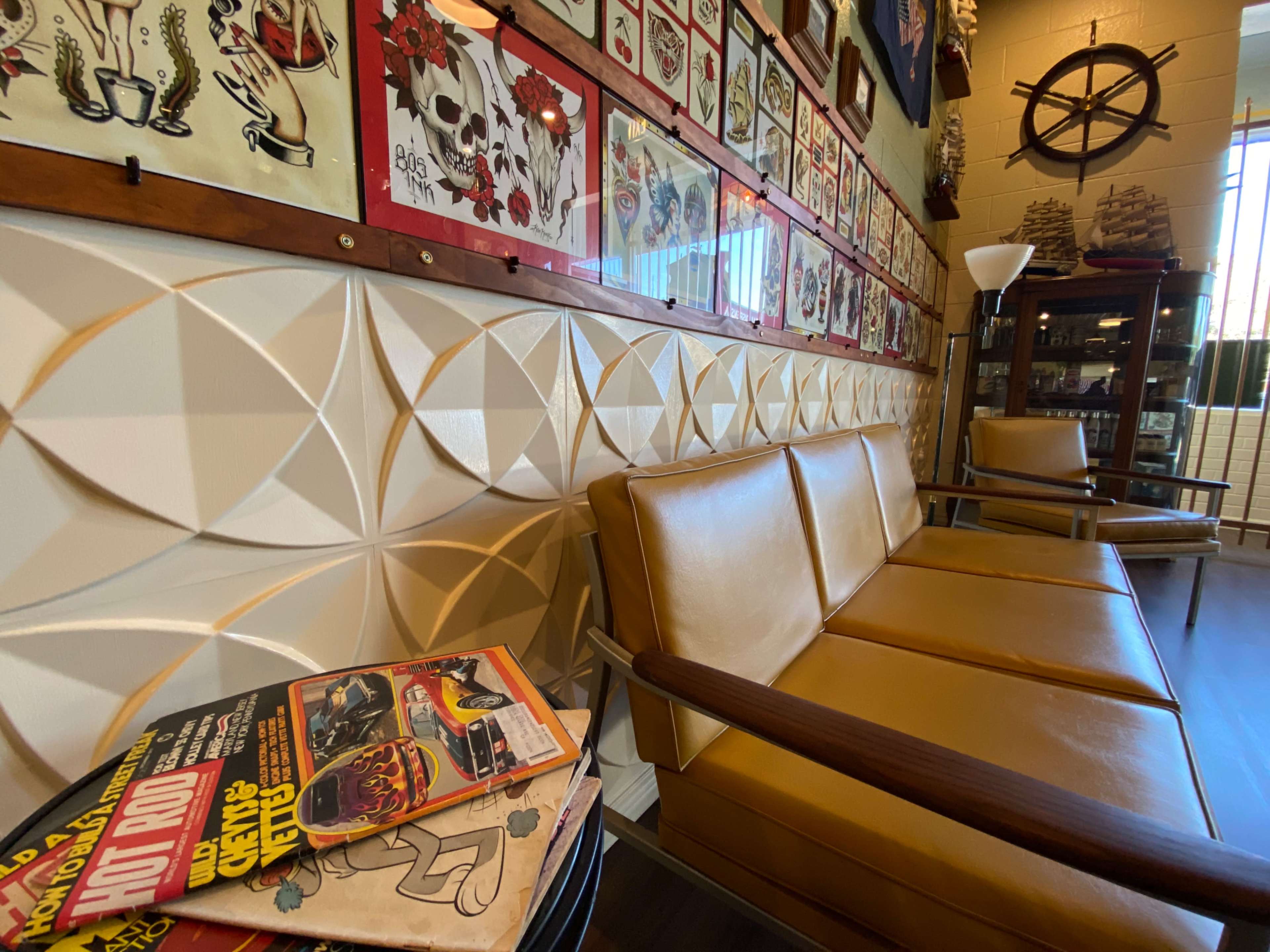 The image shows a vintage-style seating area with a textured wall, adorned with framed art, and a stack of magazines resting on the floor.