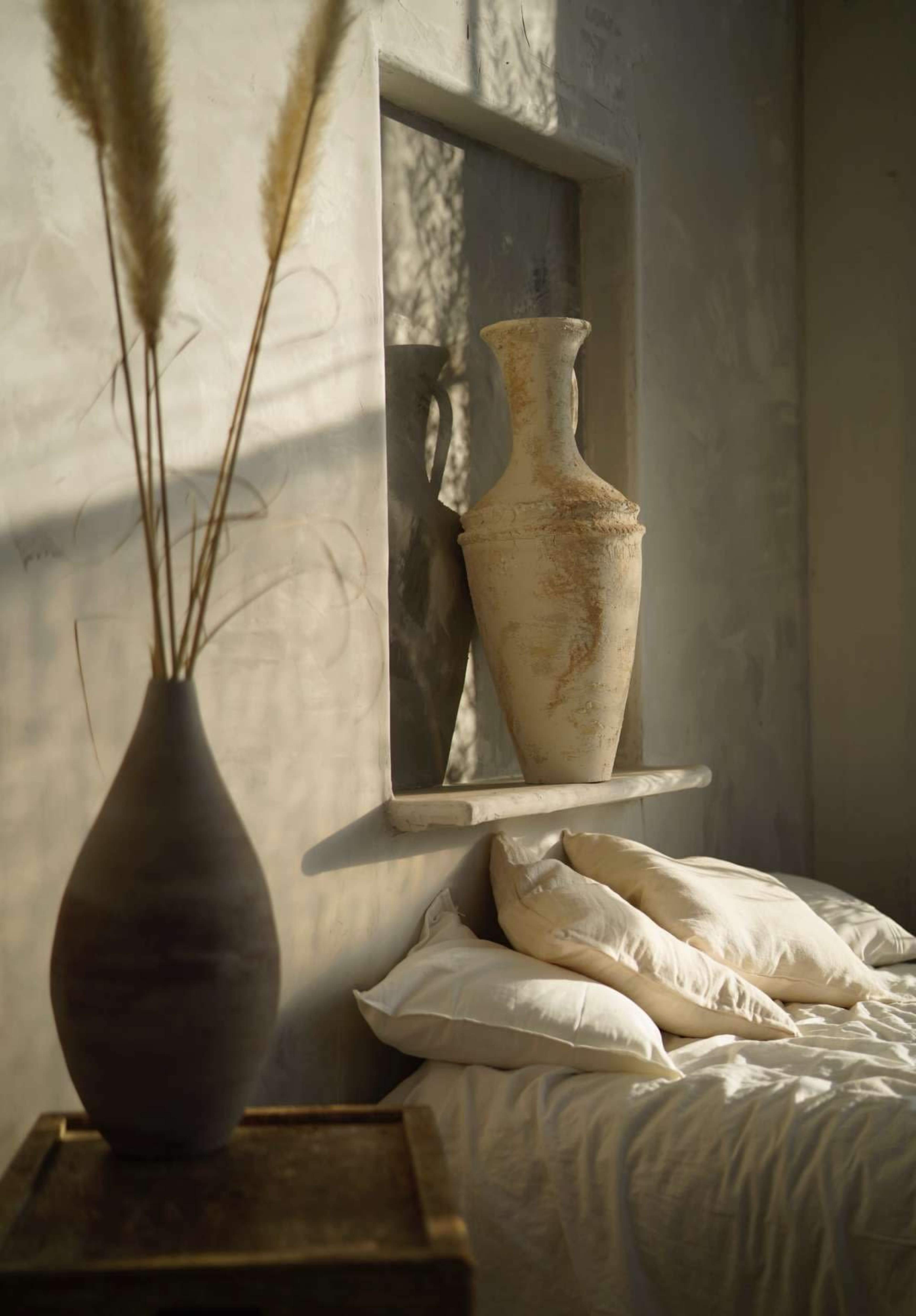 A minimalist bedroom features a bed with white pillows and two decorative vases on a ledge against a textured wall.