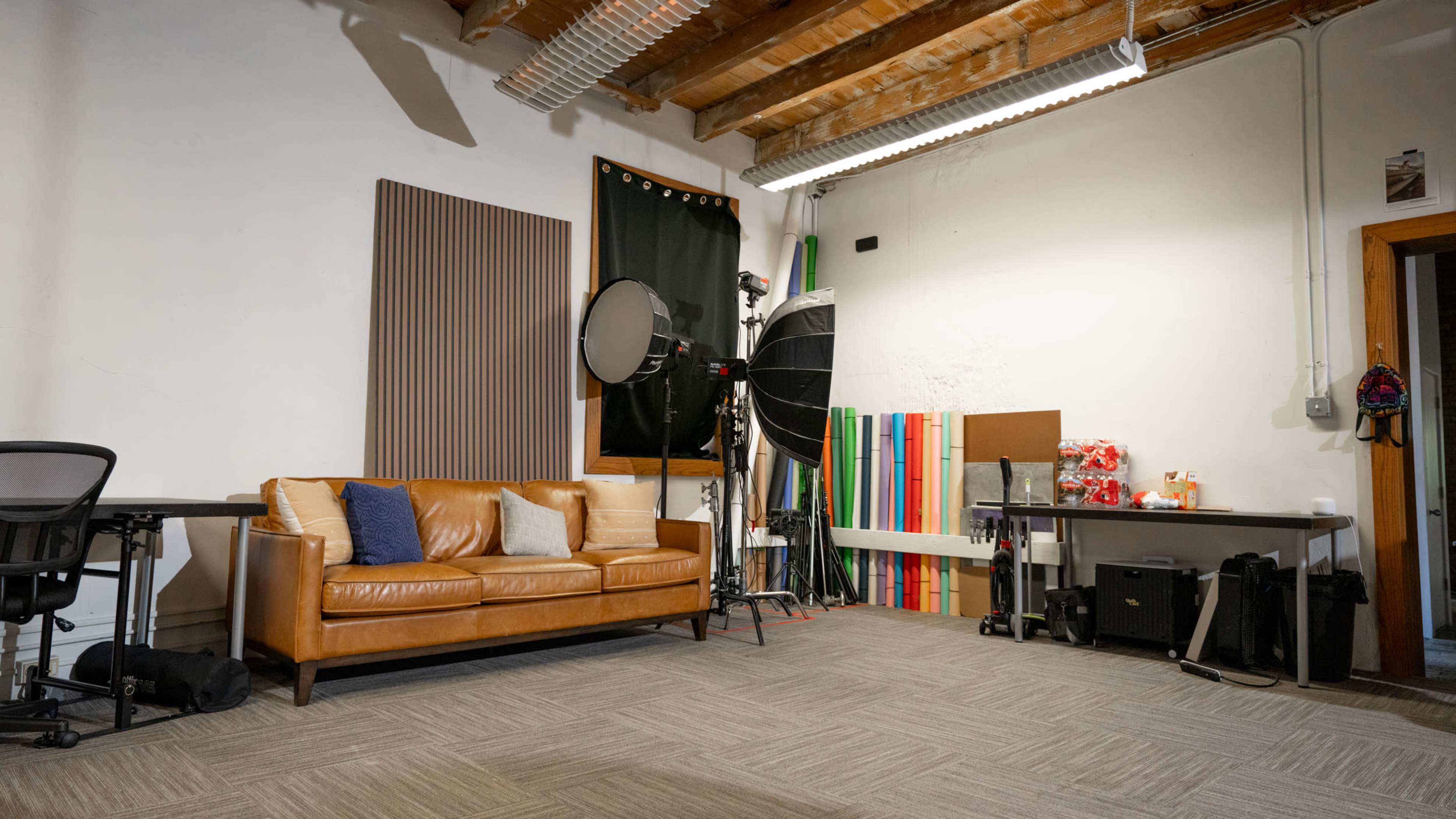 The image shows a spacious studio with a brown leather couch, photography equipment, colored backdrops, and a desk.