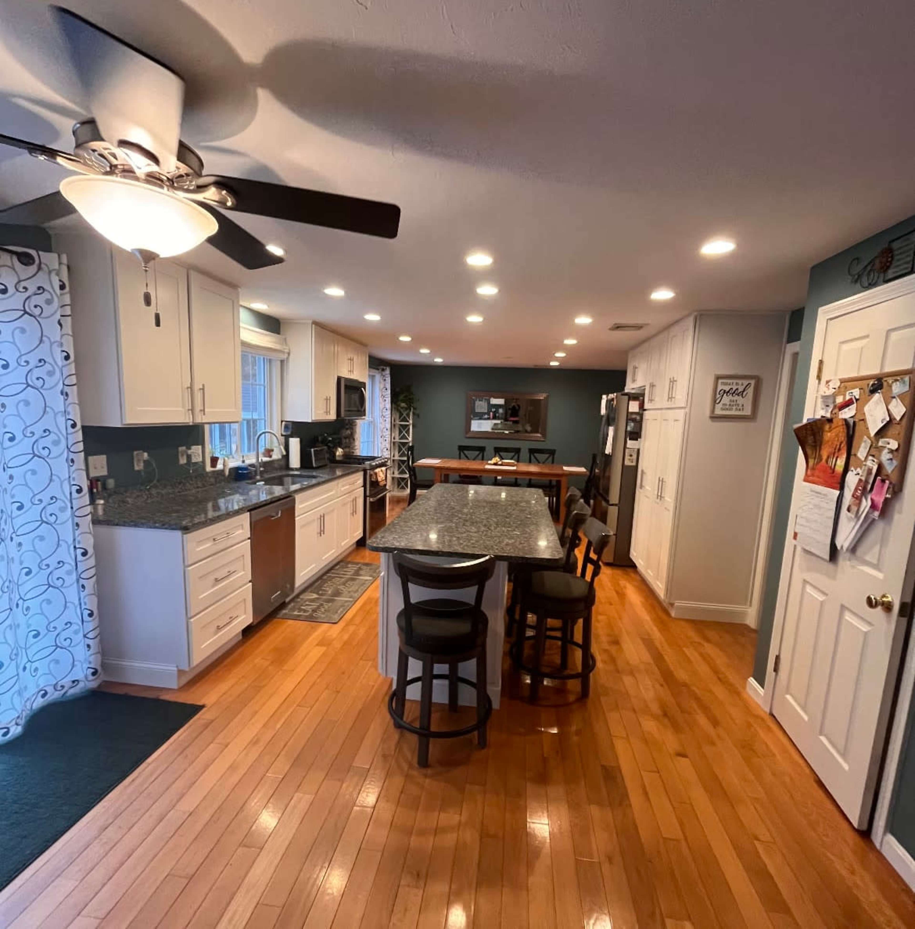 The image shows a modern kitchen with wooden floors, an island with bar stools, and stainless steel appliances.