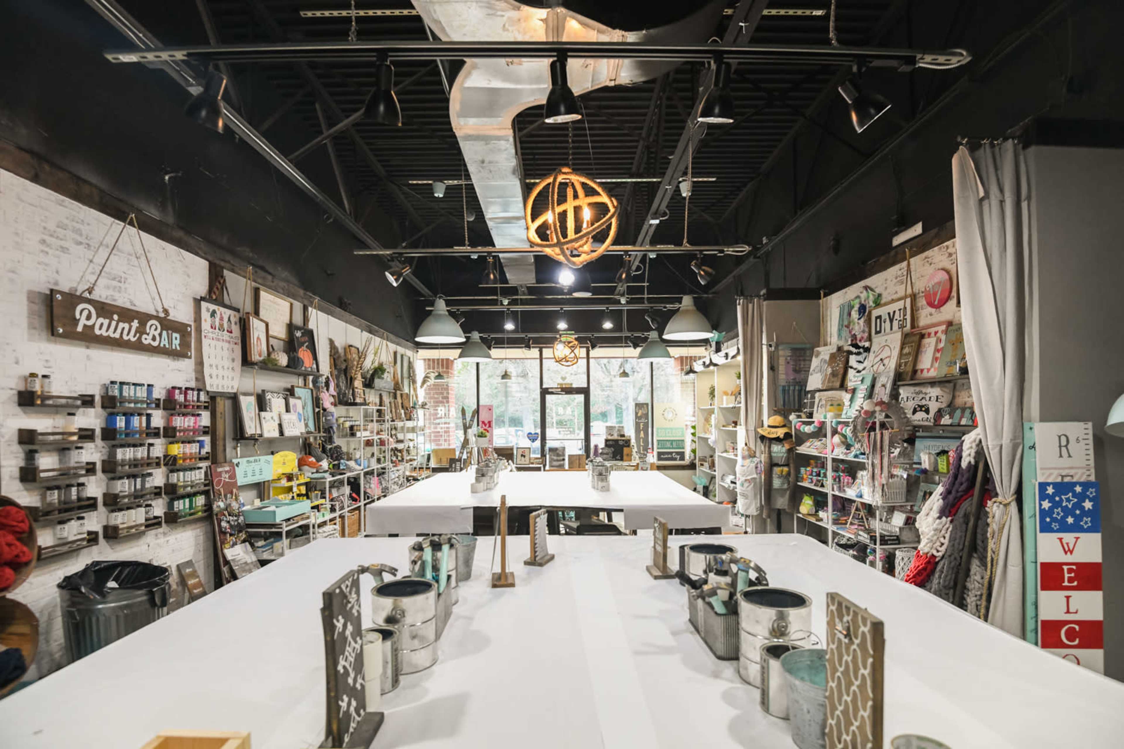 An art studio with neatly arranged tables, paint supplies, and shelves lined with craft materials.