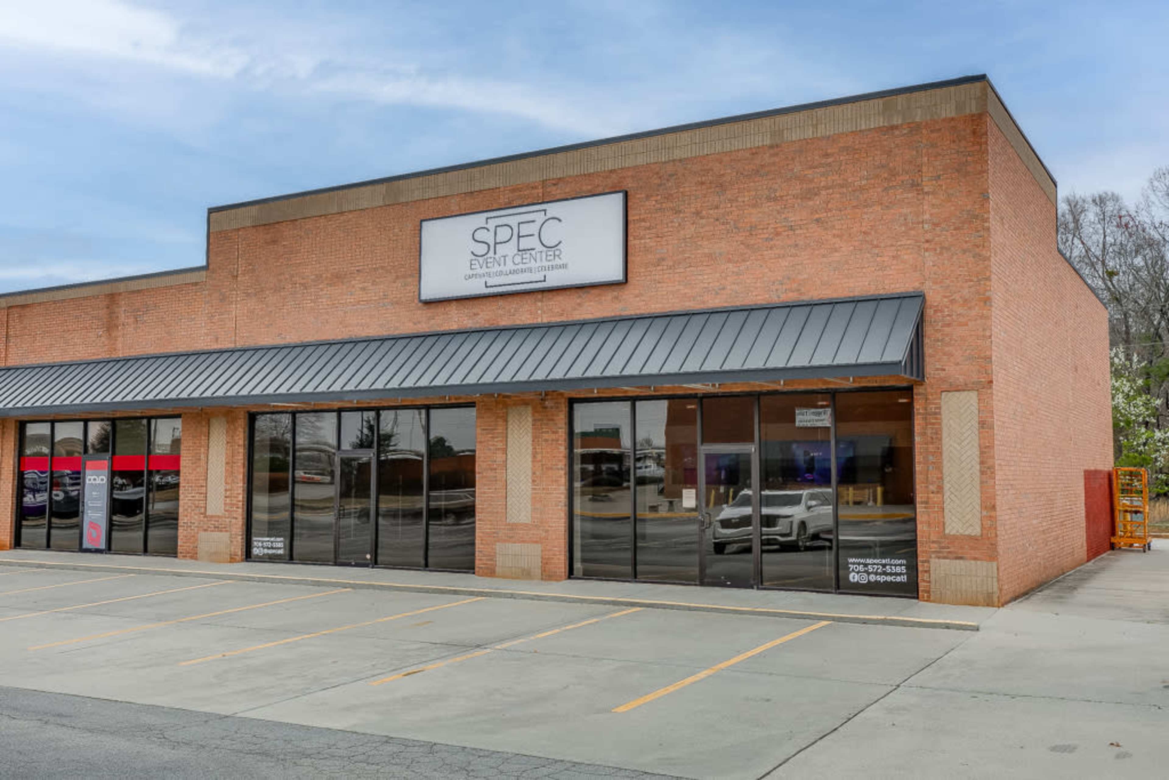 A brick building with a sign reading "SPEC EVENT CENTER" and large glass windows in front, located in a parking lot.
