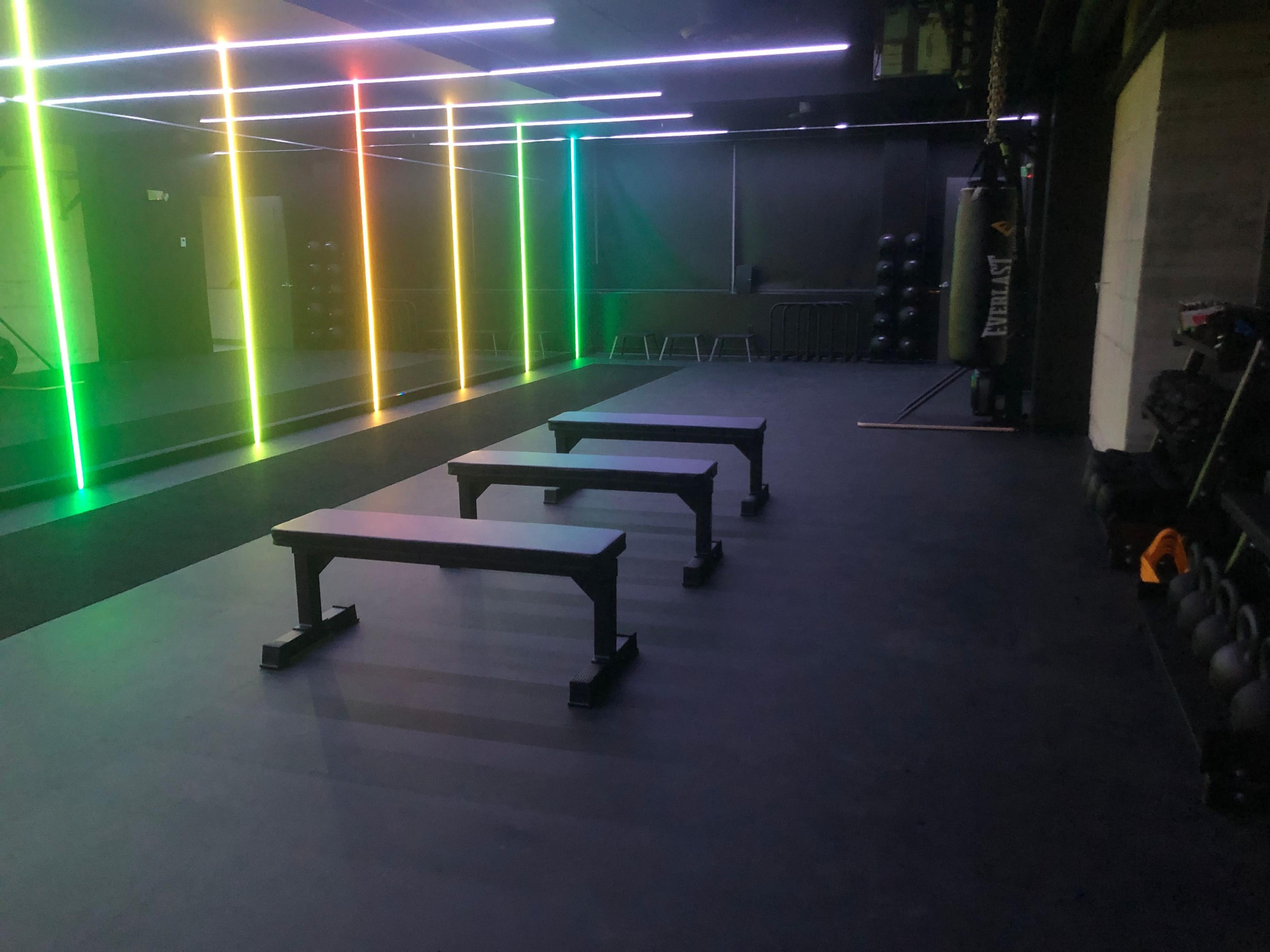 A modern gym interior with three workout benches arranged in front of a colorful illuminated wall.