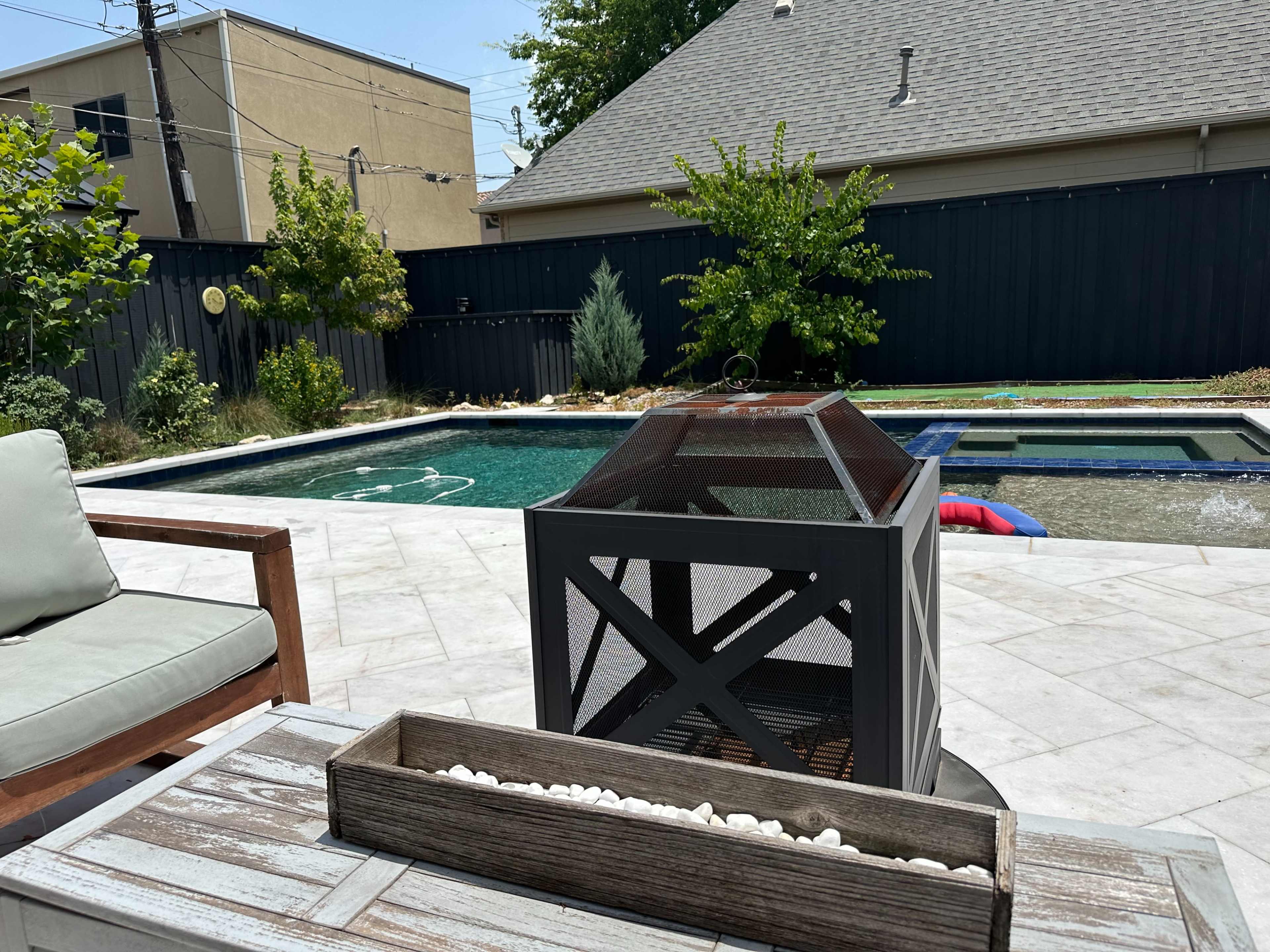 A backyard features a swimming pool surrounded by a patio, a seating area, and a fire pit.