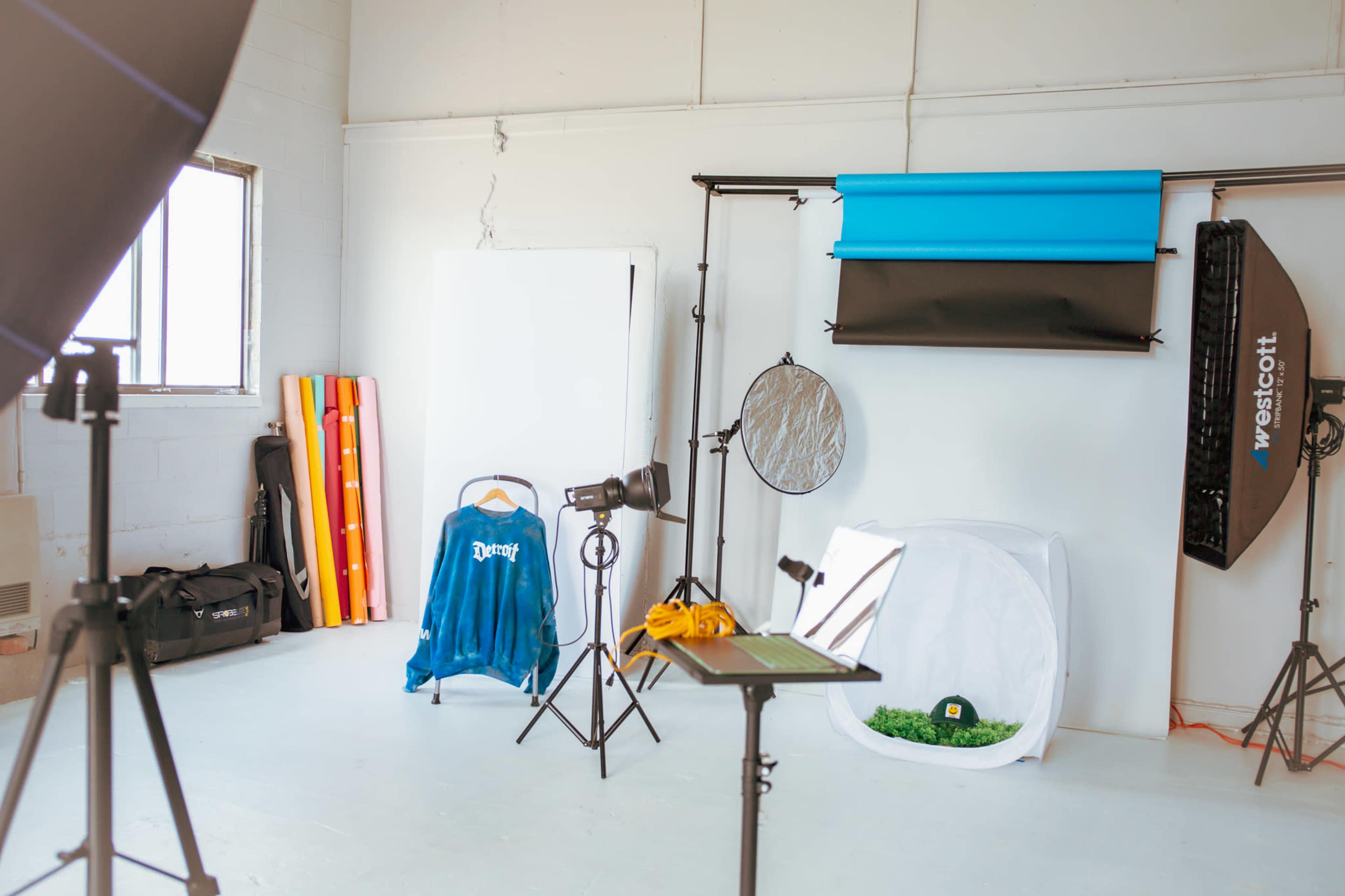 The image shows a photography studio with lighting equipment, backdrops, and props arranged in a bright, open space.