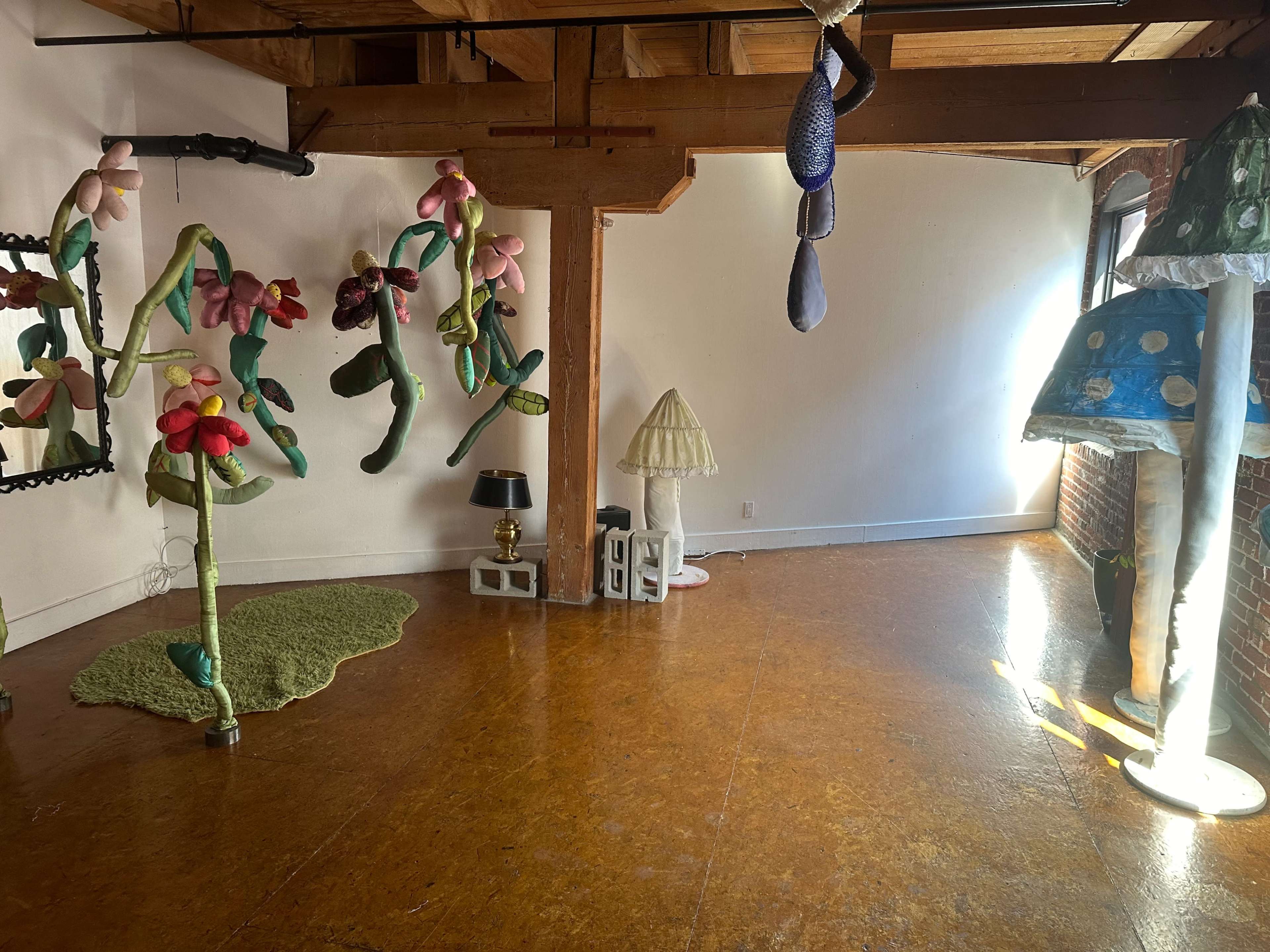The image shows a spacious room with colorful, oversized fabric flowers and whimsical light fixtures adorning the walls and corners.