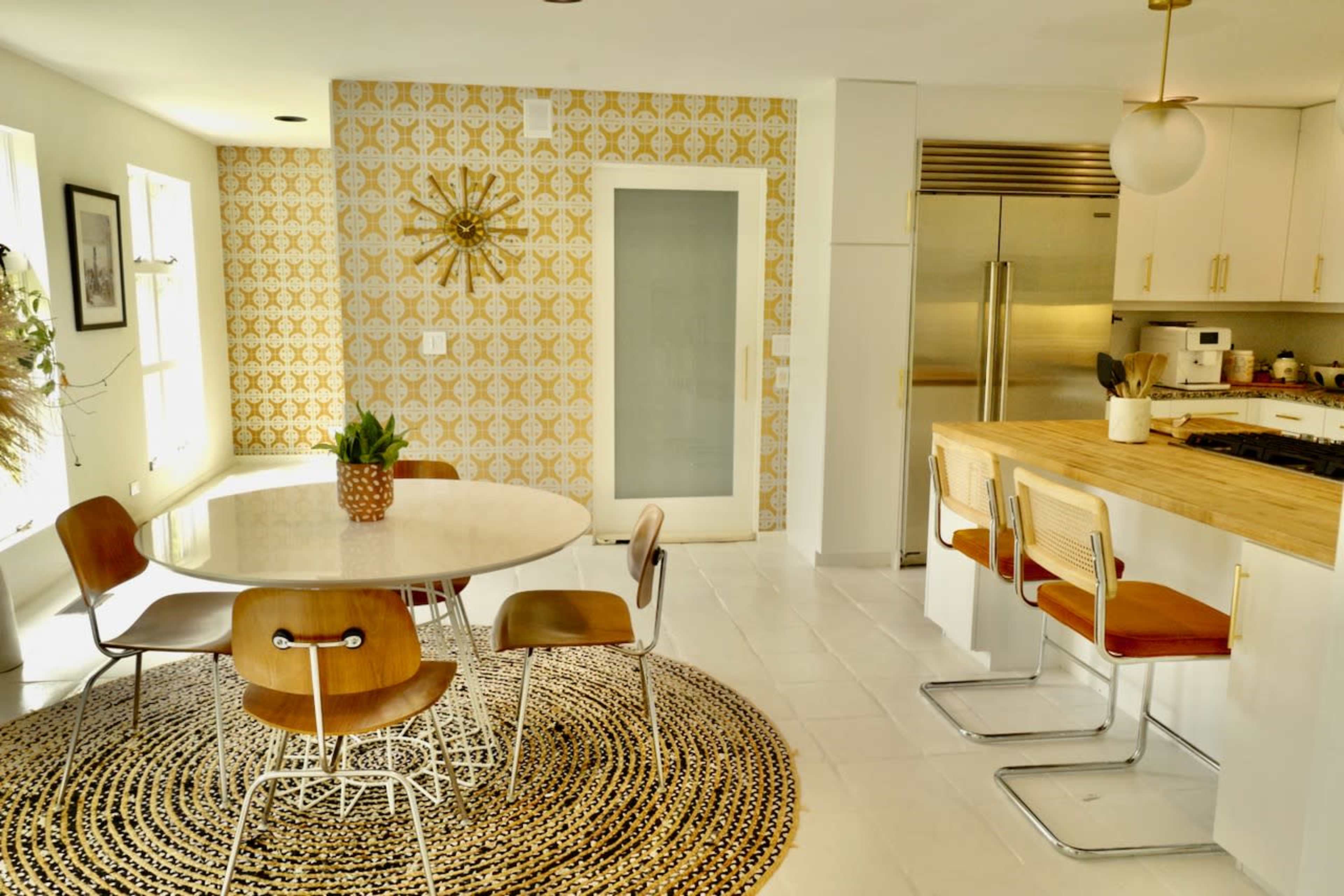 A modern kitchen features a round dining table with wooden chairs, a patterned wall, and sleek appliances.