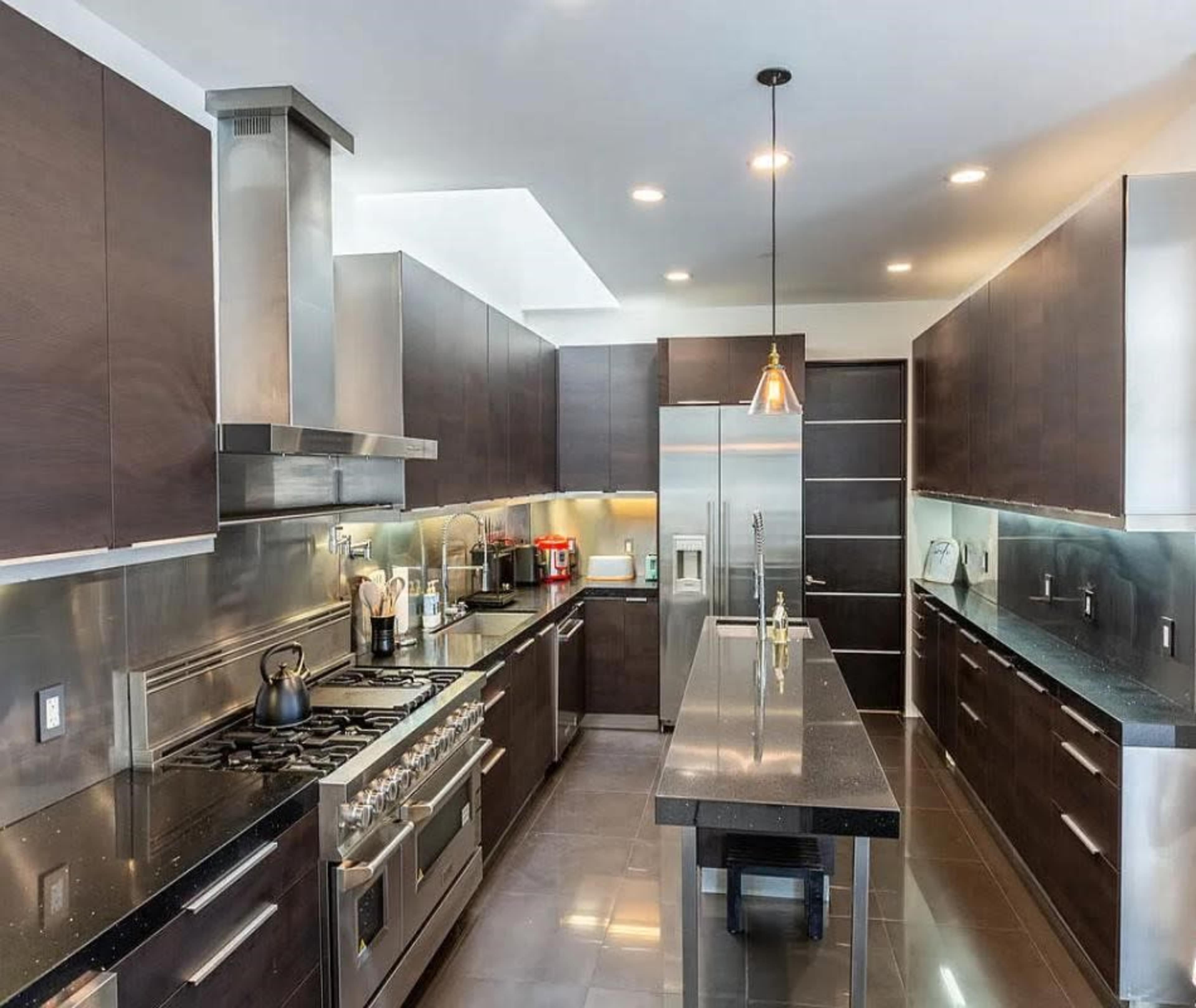 The image shows a modern kitchen with dark cabinetry, stainless steel appliances, and a central island.