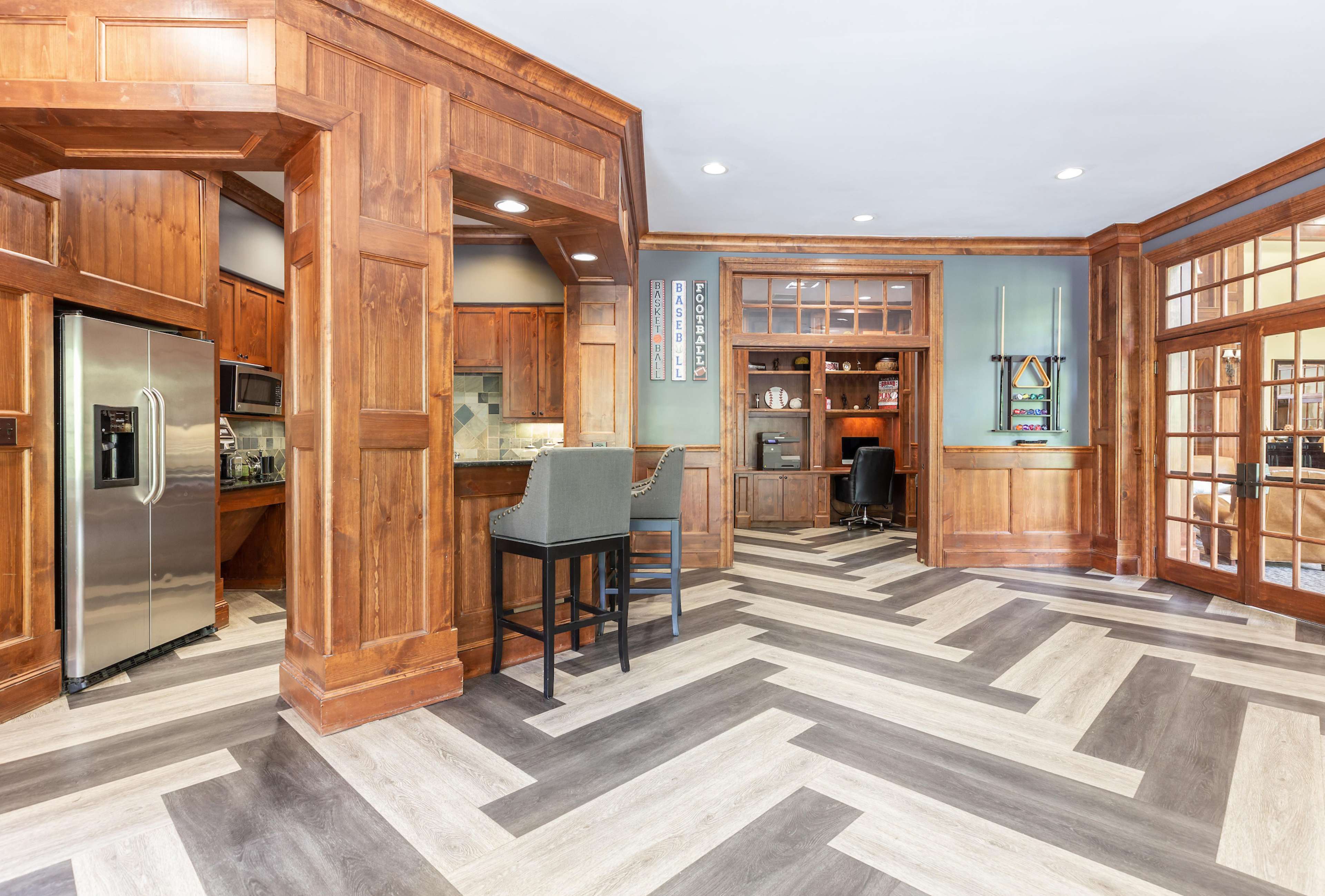 A spacious kitchen and home office area with hardwood cabinetry, stainless steel appliances, and a herringbone-patterned floor.