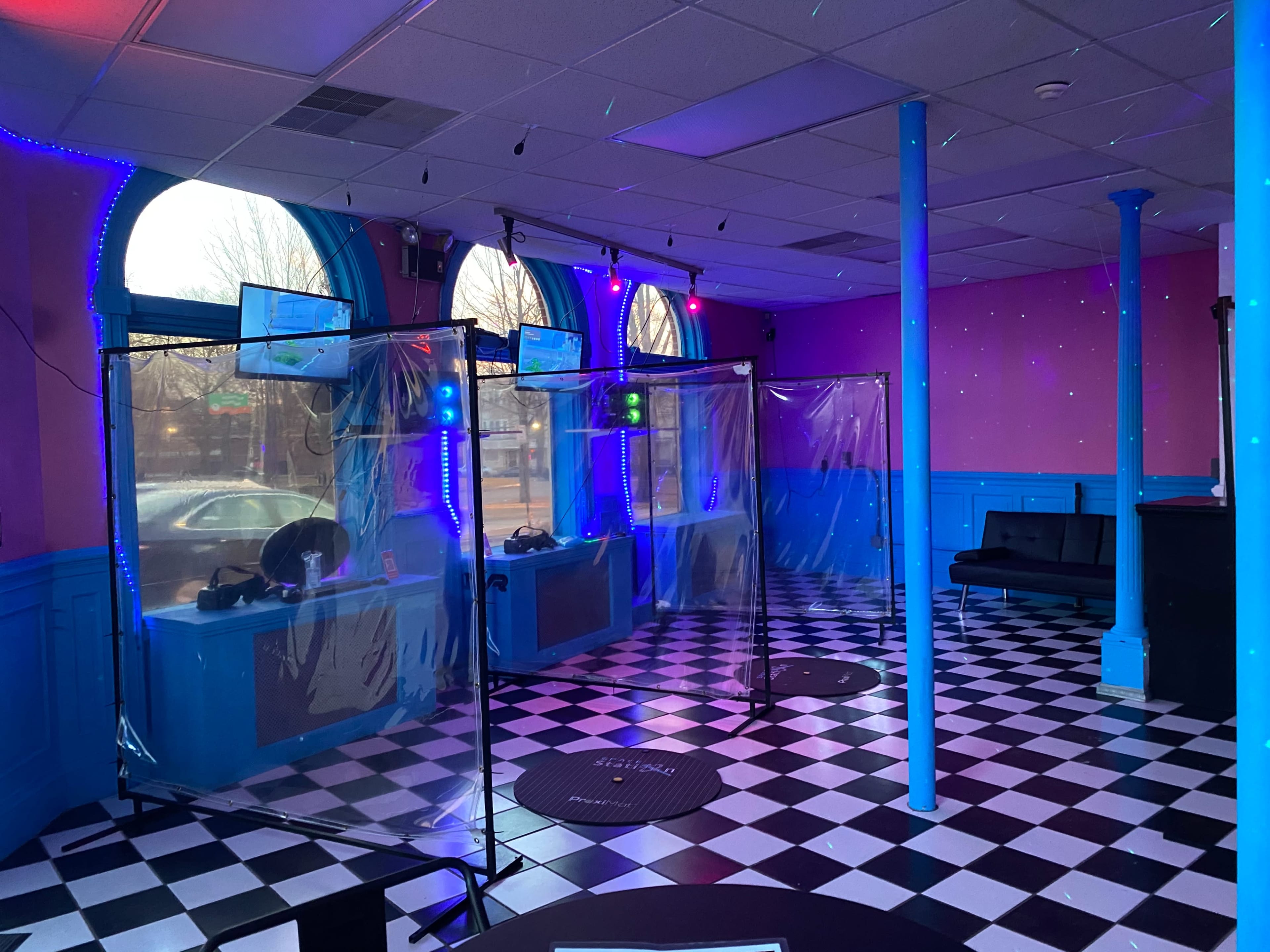 The interior of a dance studio features plastic barriers separating spaces, with colorful lighting and a checkerboard floor.