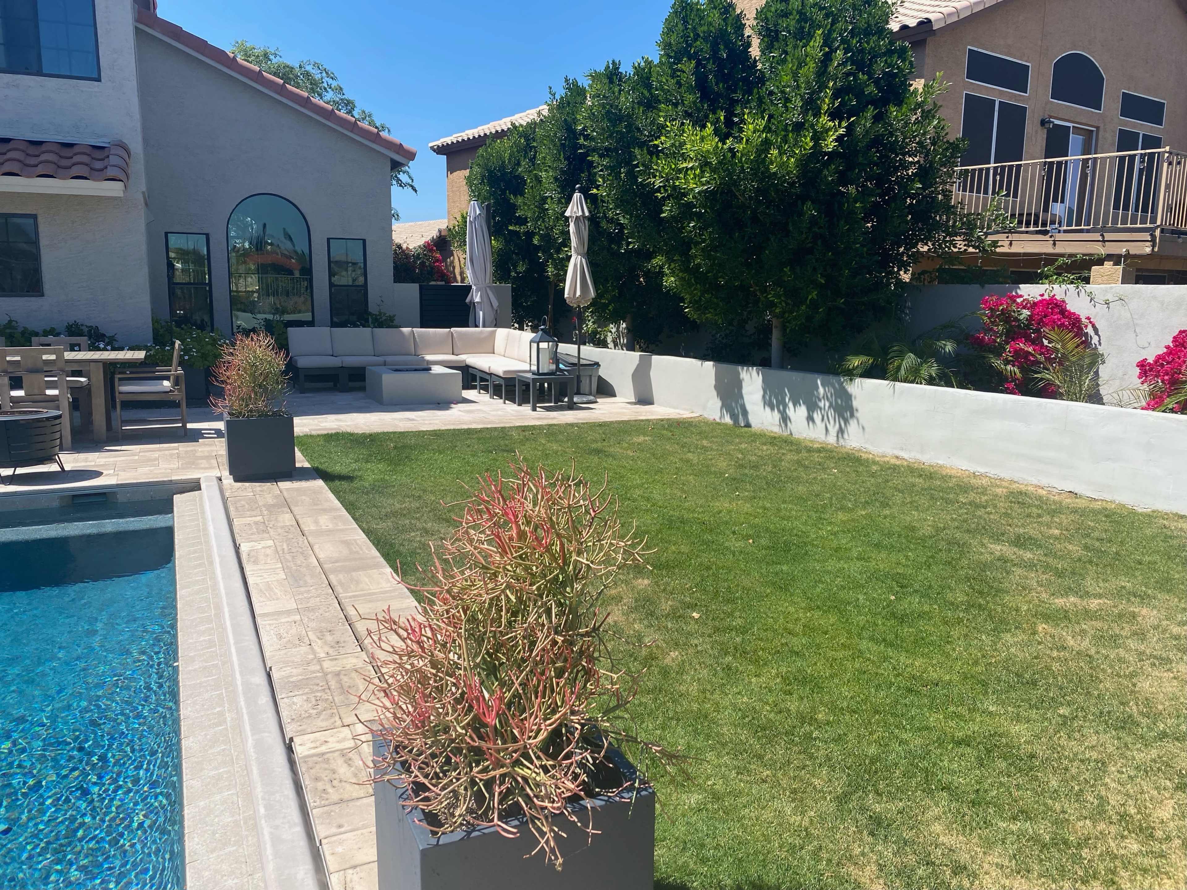 A well-maintained backyard features a swimming pool, a patio area with seating, and neatly trimmed grass bordered by planters.